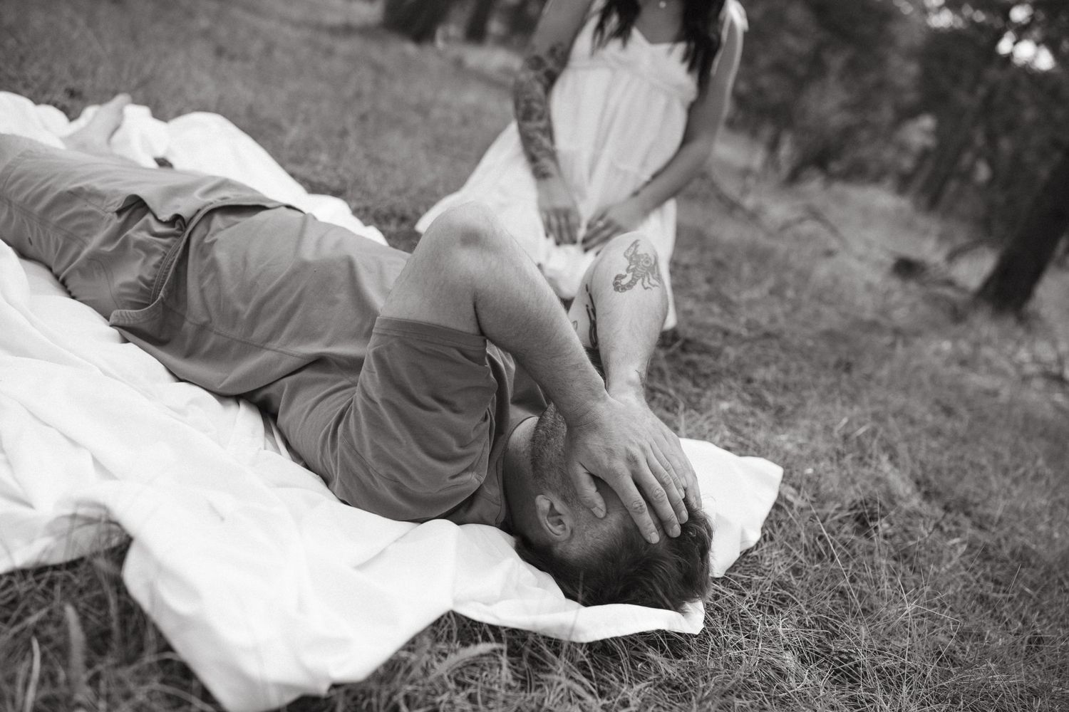 Black and white photo of couple laying on blanket during outdoor spiritual ceremony.