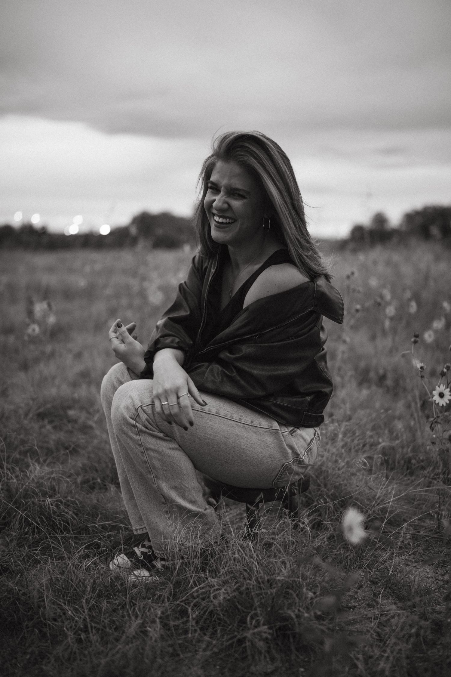 A series of black and white photos showing someone laughing joyfully while sitting in a wildflower meadow.