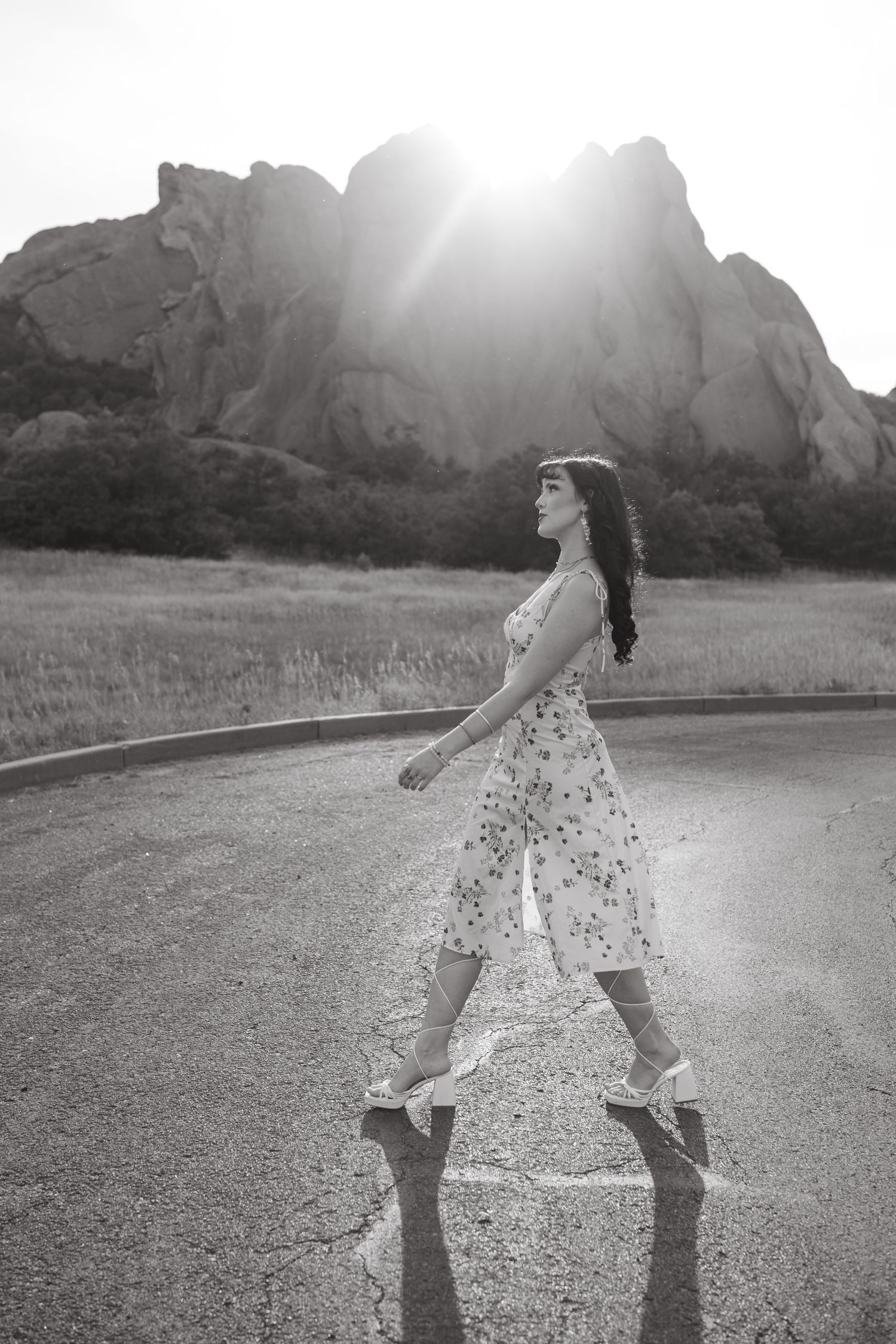 A person in a polka dot dress walks along a winding mountain road in black and white.