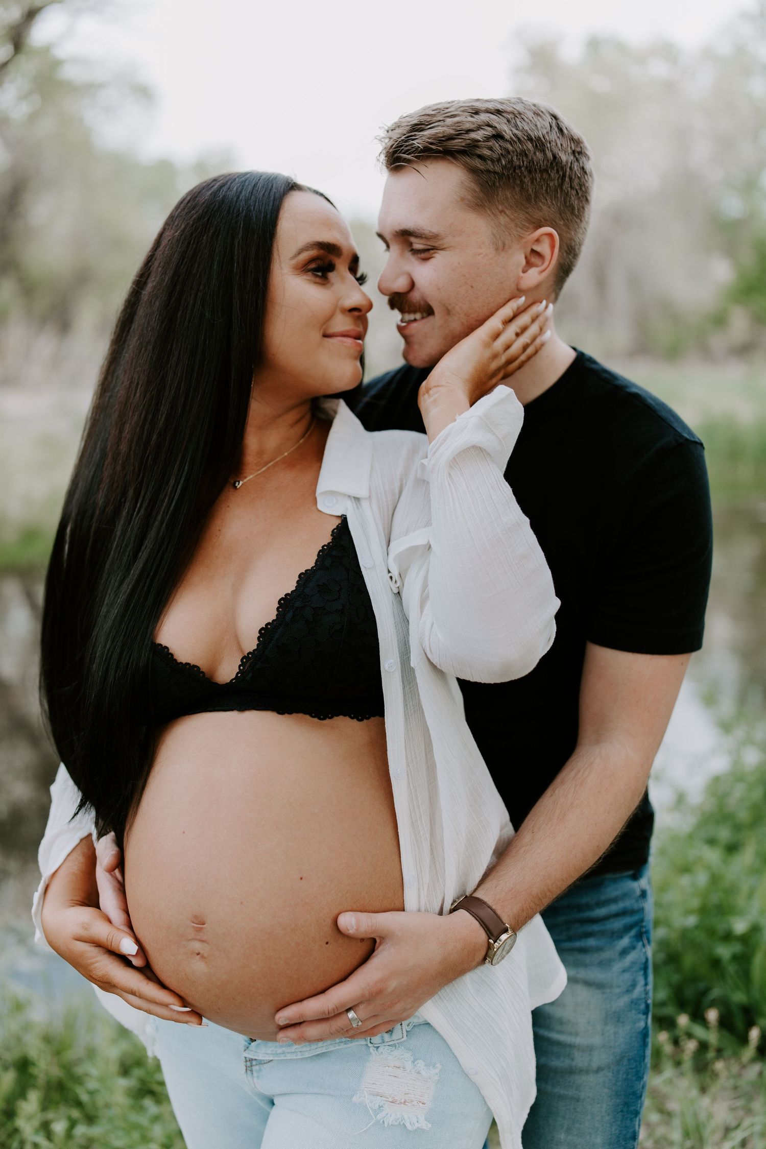 An intimate maternity portrait of an expecting couple outdoors in casual attire.