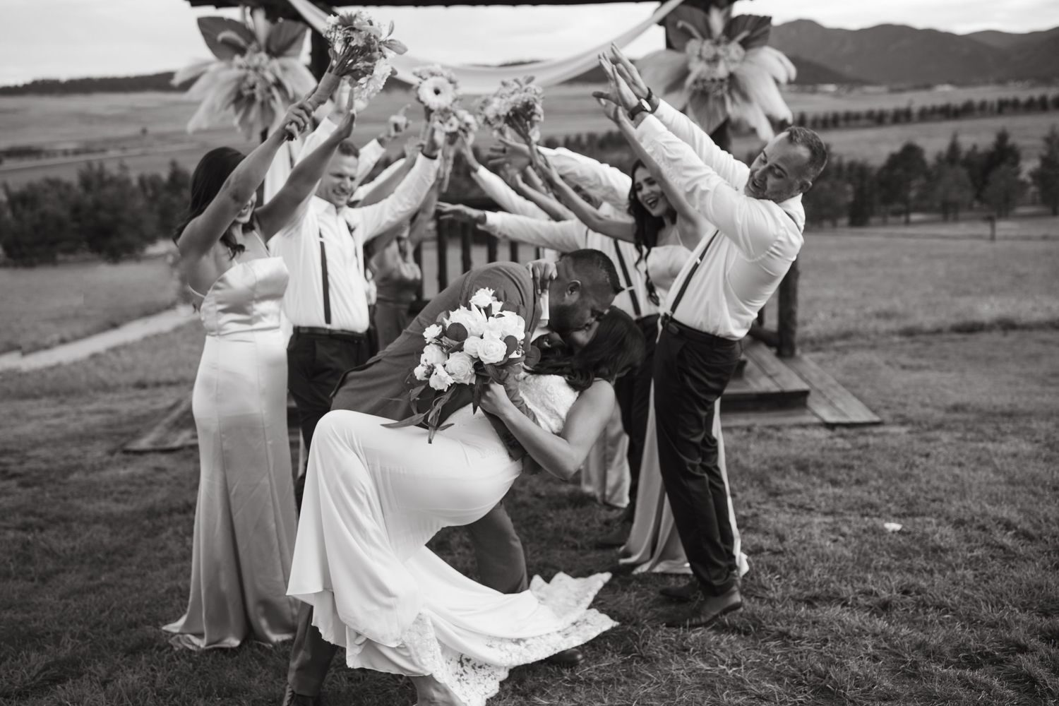 A playful black and white photo of wedding party members creating heart shapes with their arms.