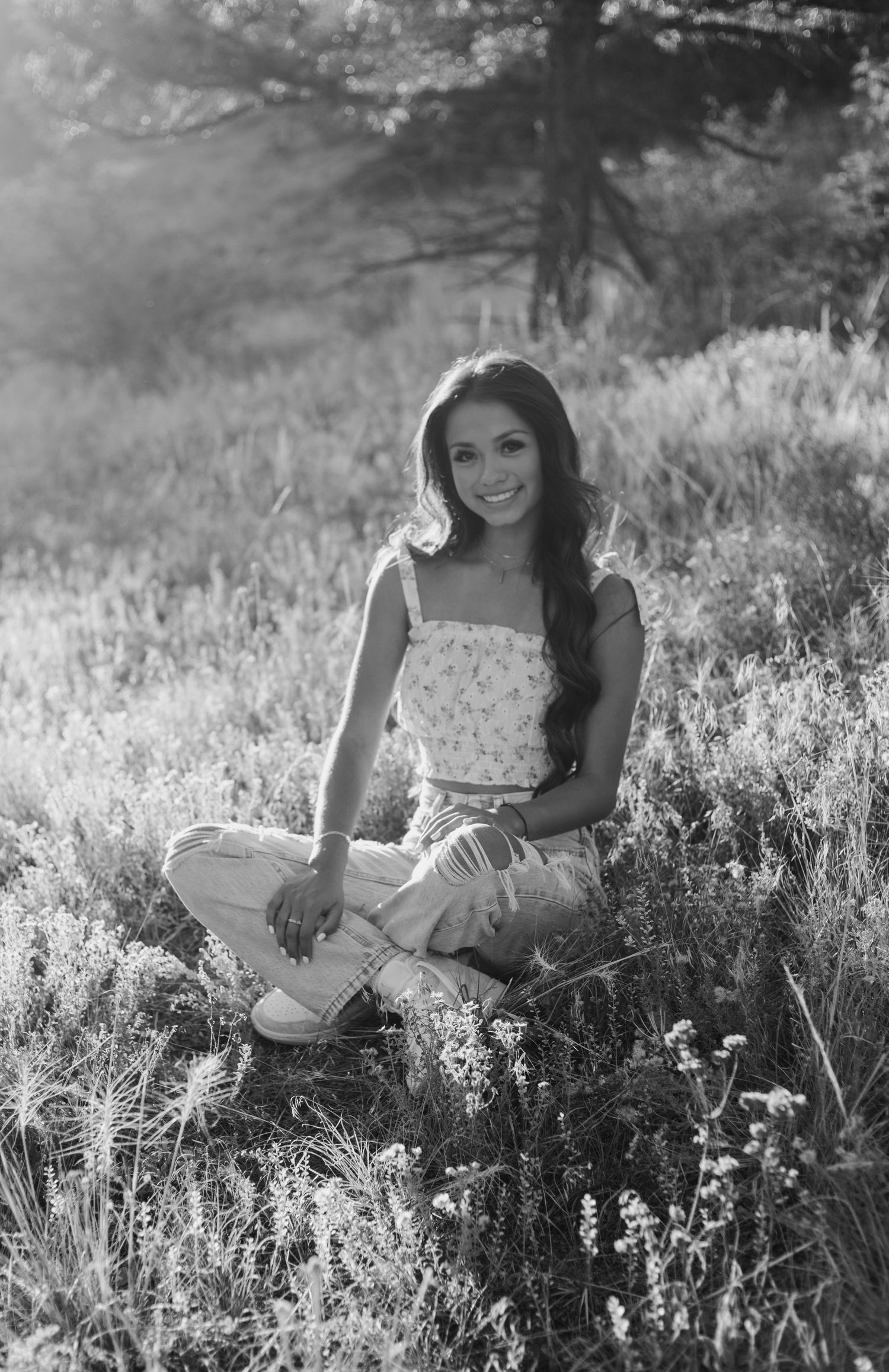 Black and white portrait in mountain meadow wearing white top and light pants.