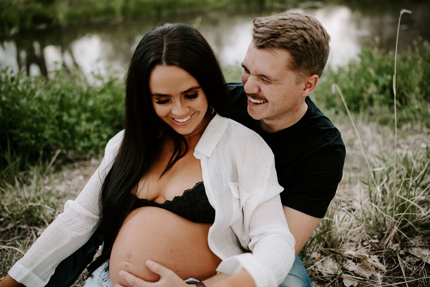 Casual maternity photo of couple by riverside in contrasting black and white outfits.