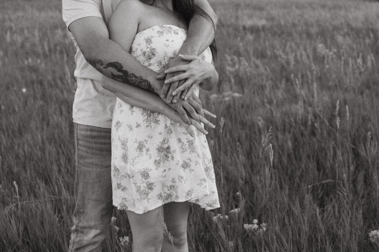 Black and white photo of couple holding each other close in a grassy field.