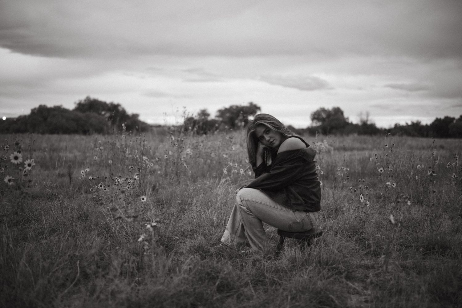 A black and white photo series showing a person crouching in a field of tall grass and wildflowers.