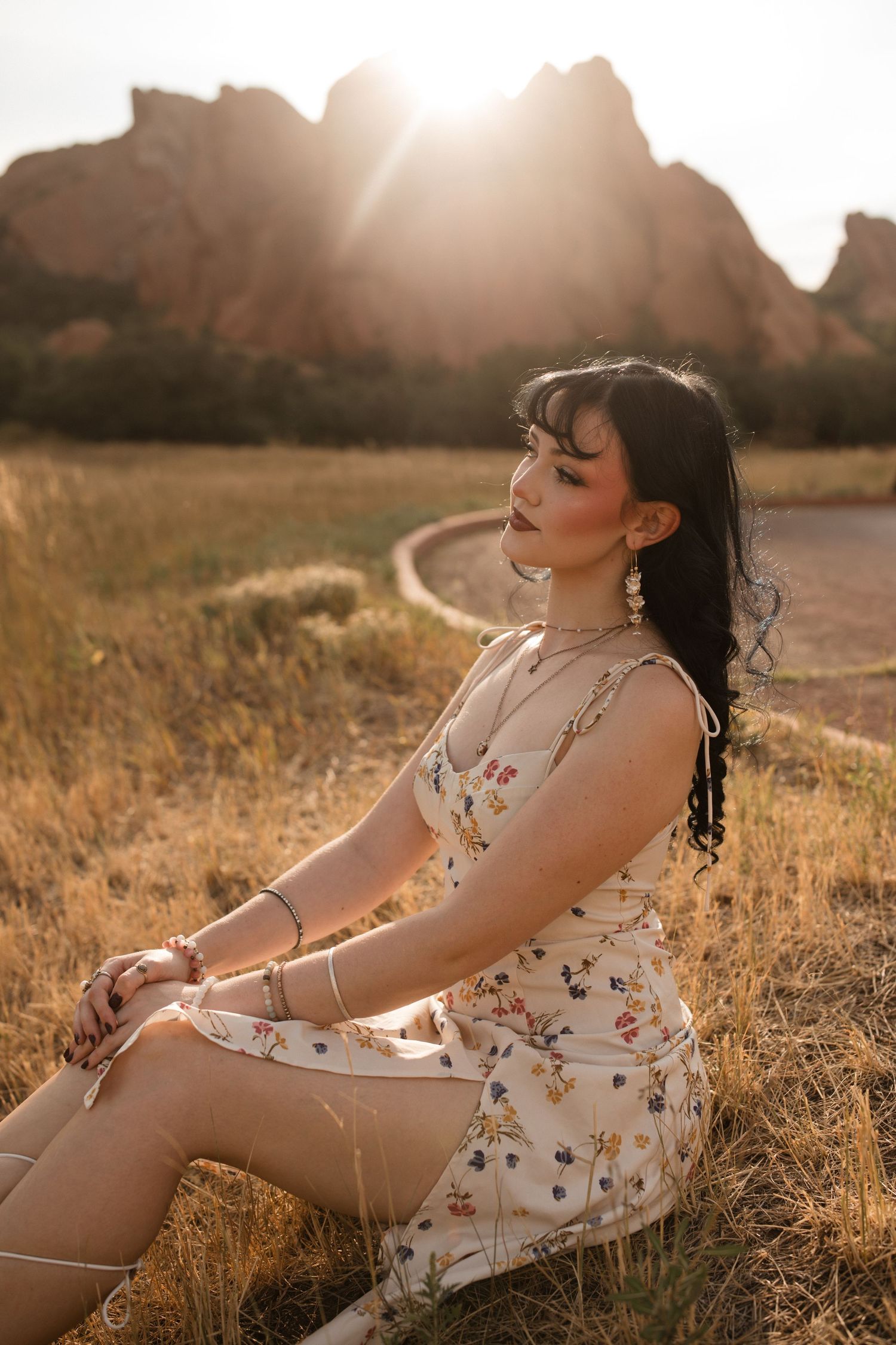 A woman in a floral dress poses gracefully in a sunlit field during golden hour.
