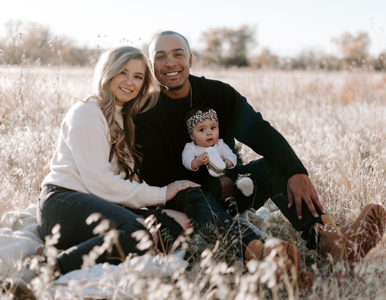 Family sitting together in a sunny winter field with a small baby wearing a sparkly crown.