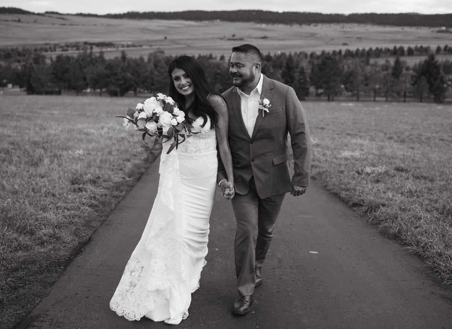 Wedding couple walking along a scenic path with rolling hills in the background.