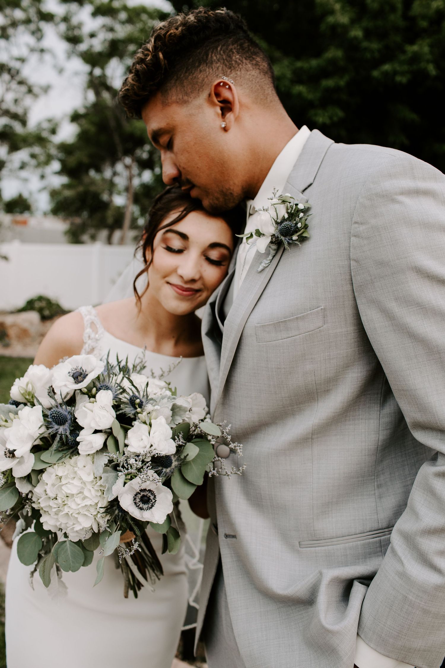 A romantic wedding photo showing a couple in gray and white embracing with a beautiful white and green floral bouquet.