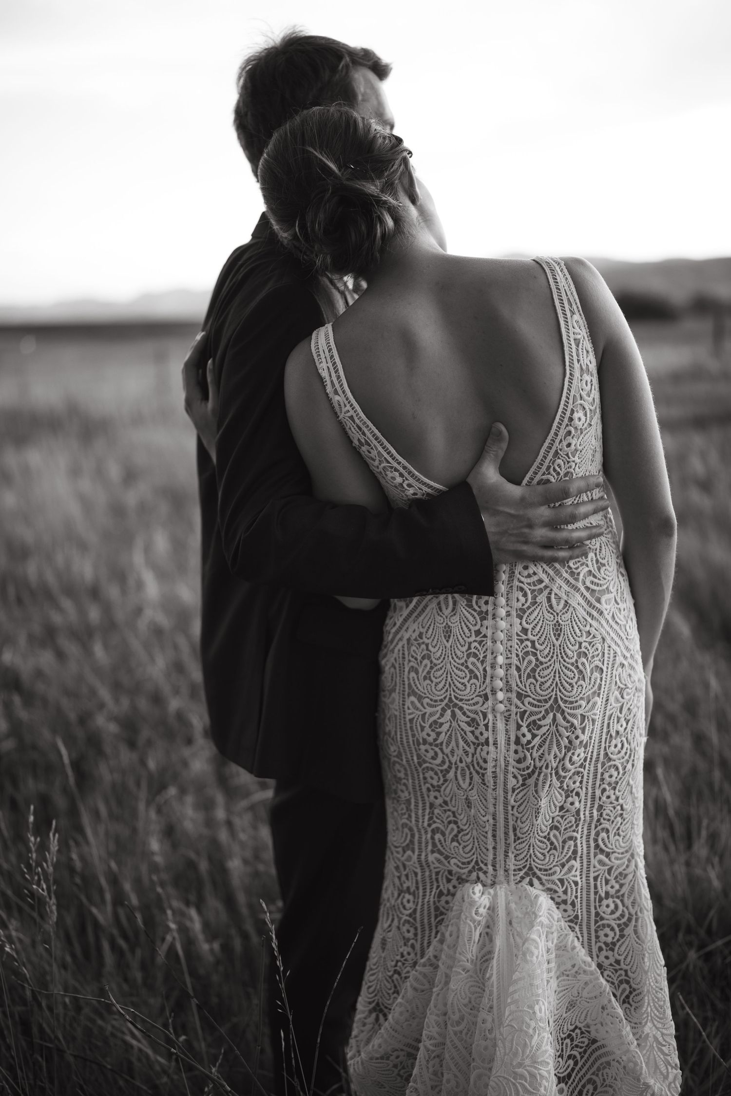 Black and white photo of couple embracing in field wearing formal attire.