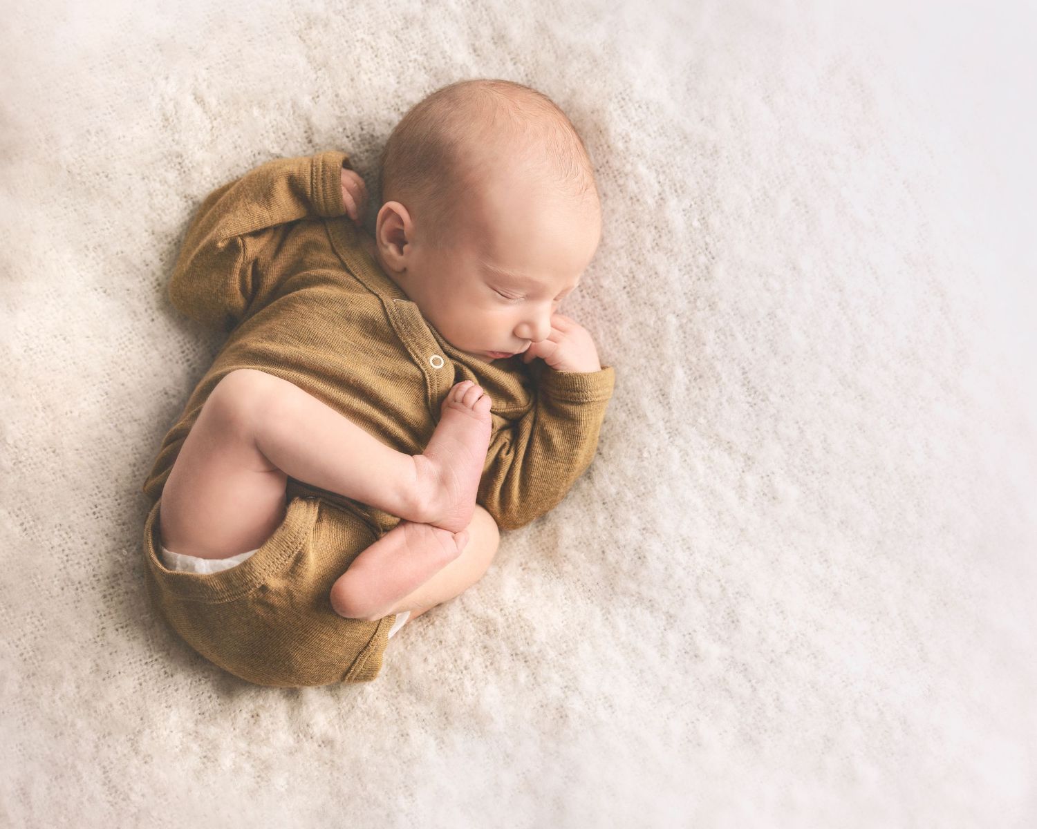 Sleeping baby wearing tan outfit on cream textured background.
