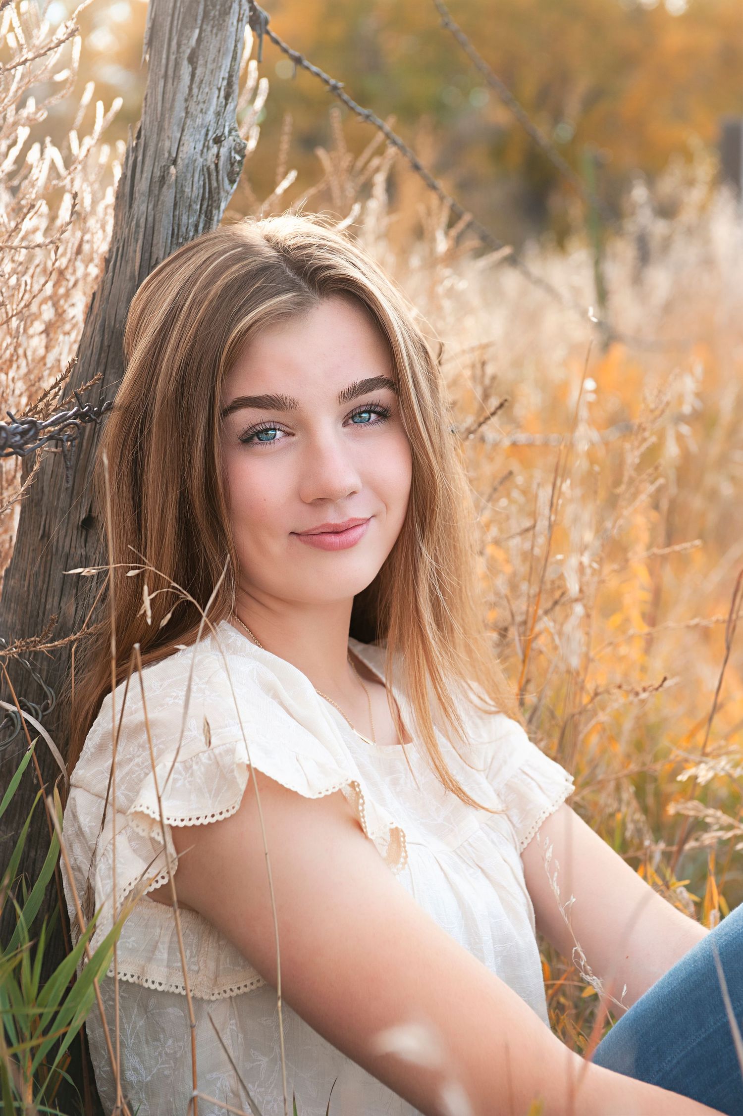 Portrait in autumn field with rustic fence and golden light.