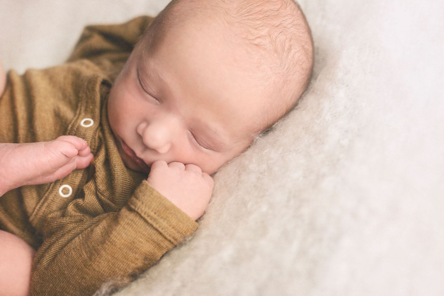 Side view of sleeping infant in tan outfit against white textured background.