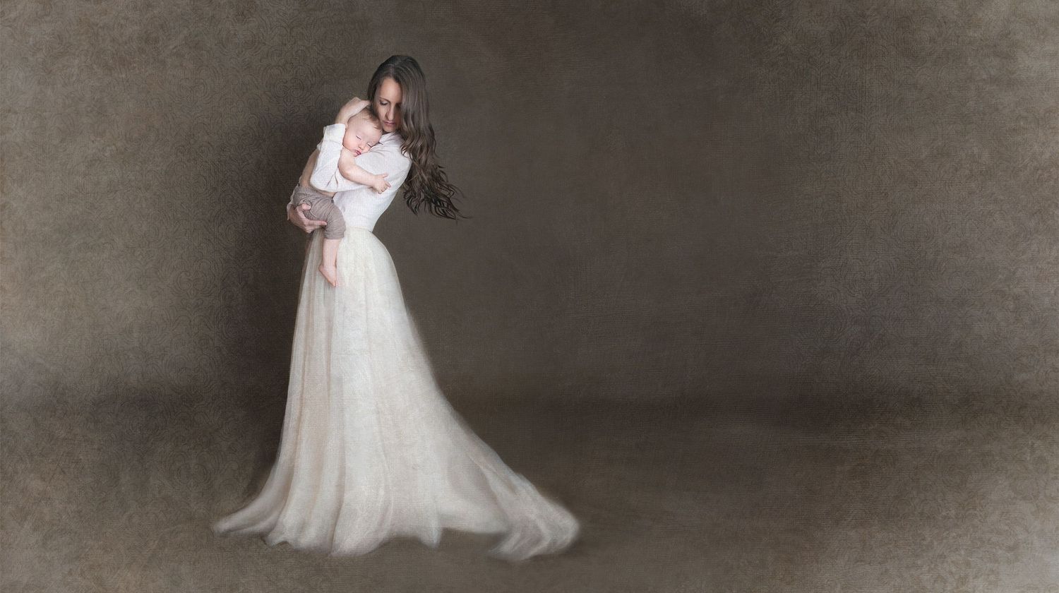 Romantic portrait of a bride in flowing white gown against muted grey backdrop.