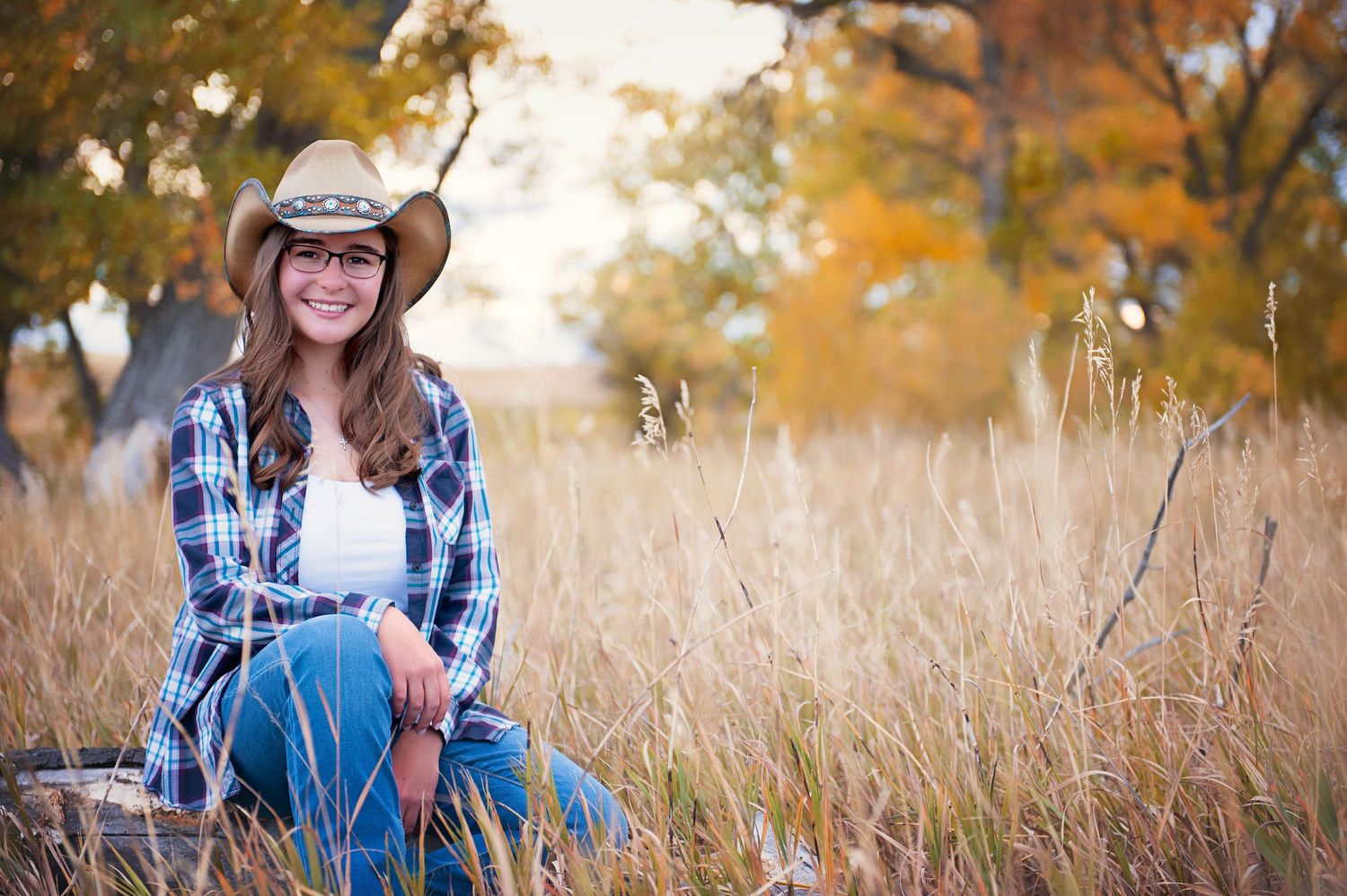 Country western portrait in plaid shirt sitting among tall autumn grass.