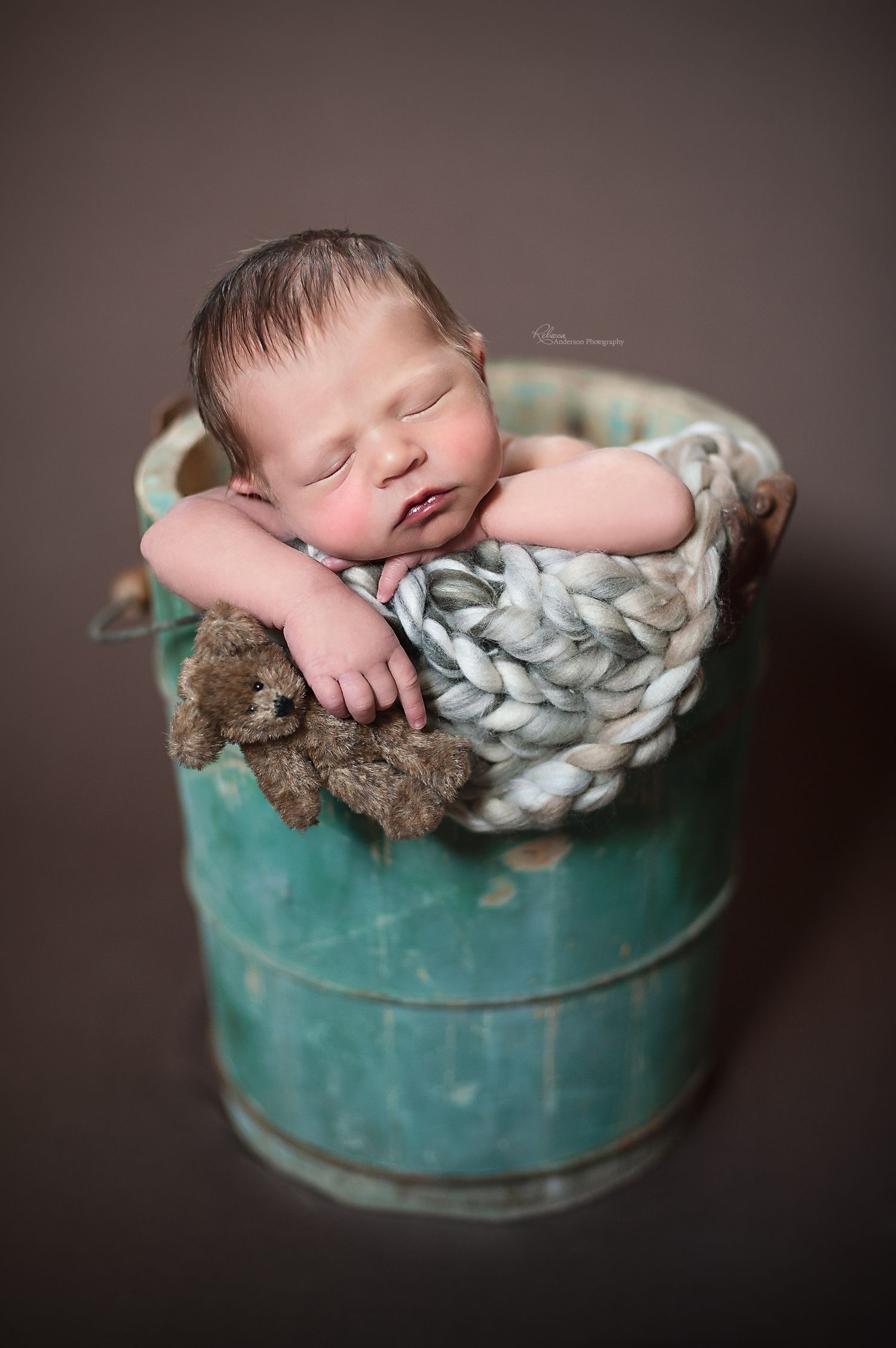 Newborn peacefully sleeping in turquoise vintage bucket with chunky knit blanket.
