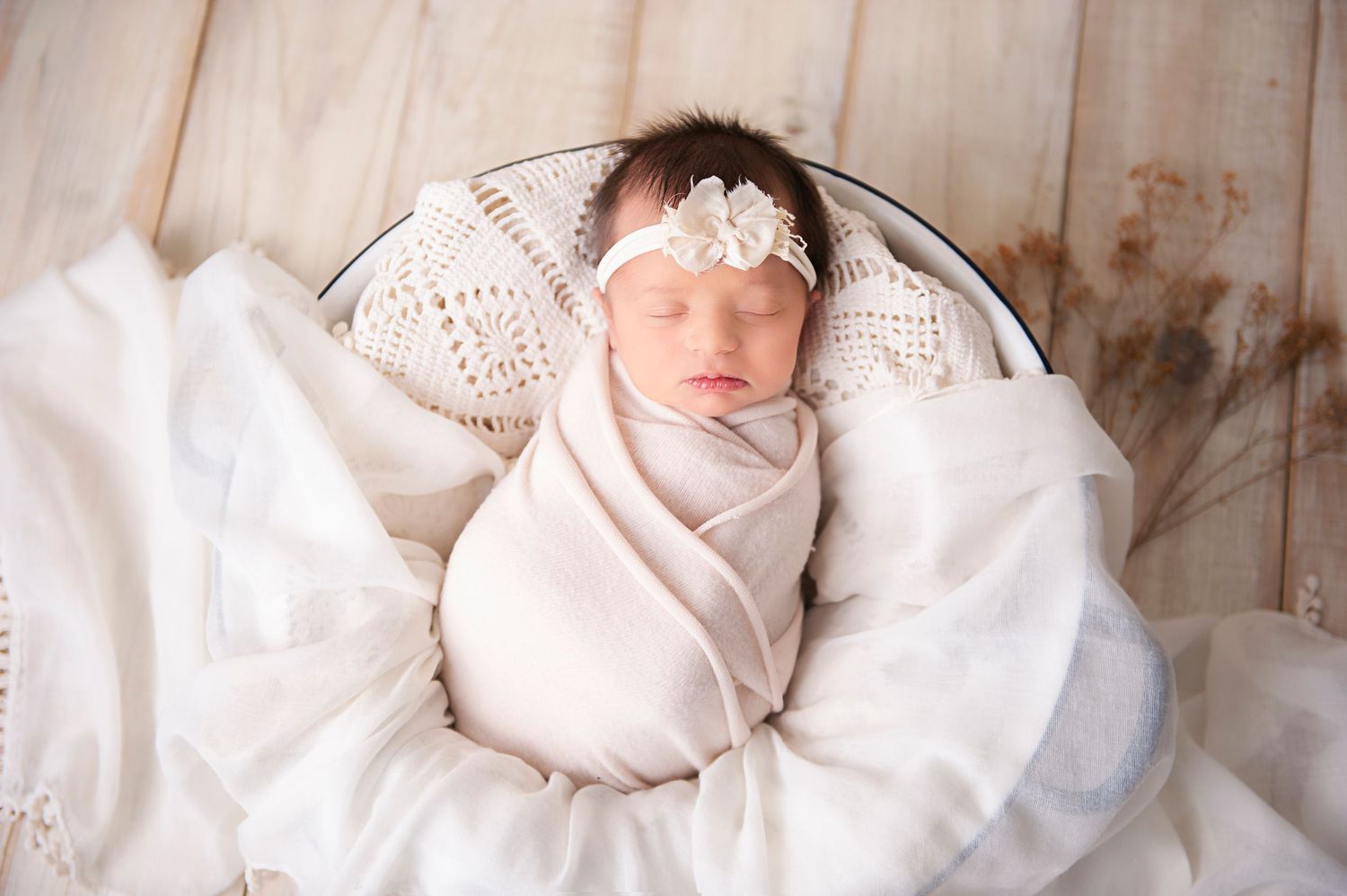 Newborn sleeping in white lace basket with delicate headband and soft wrap.