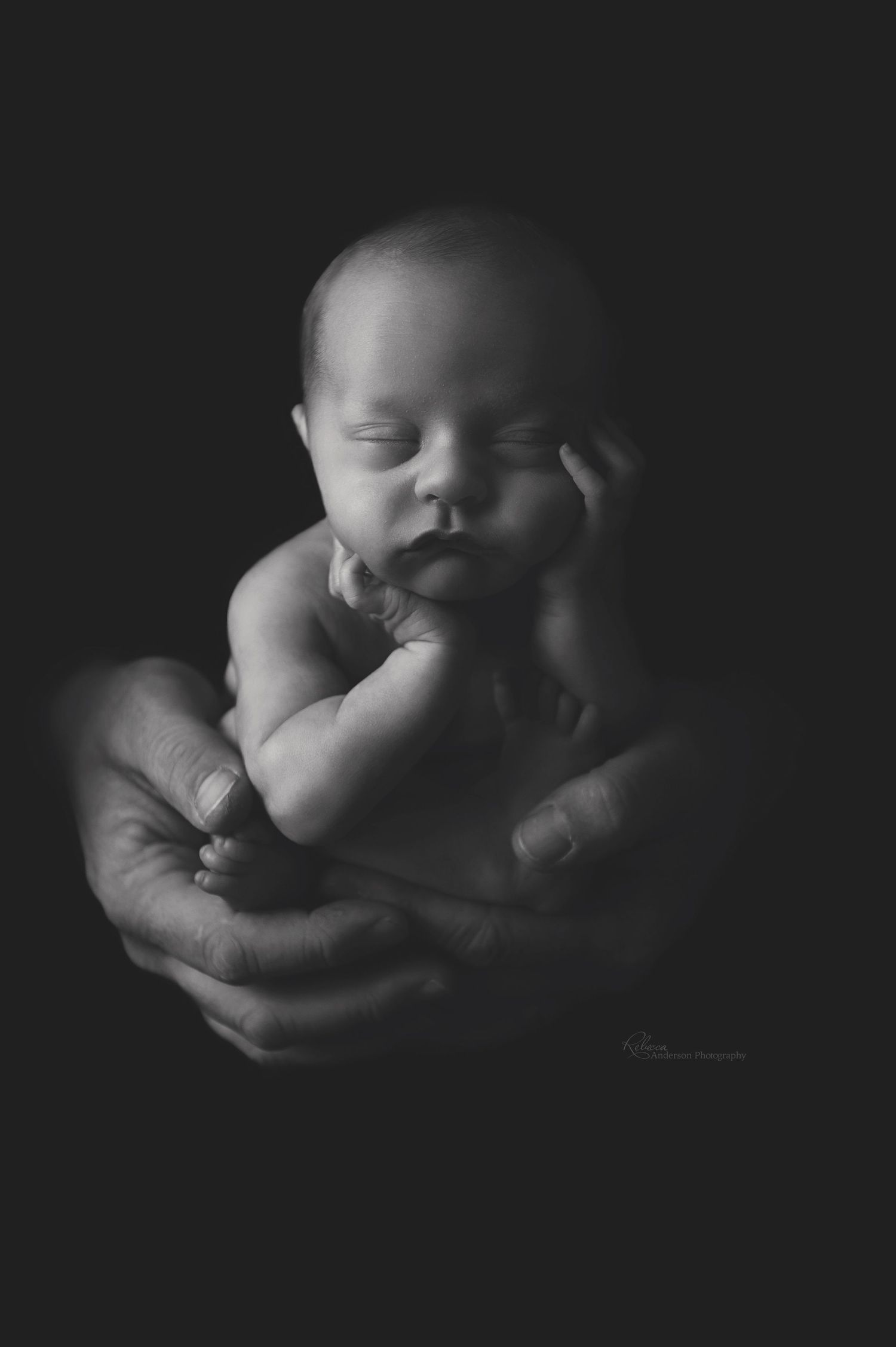 Dramatic black and white portrait of sleeping newborn cradled in gentle hands.