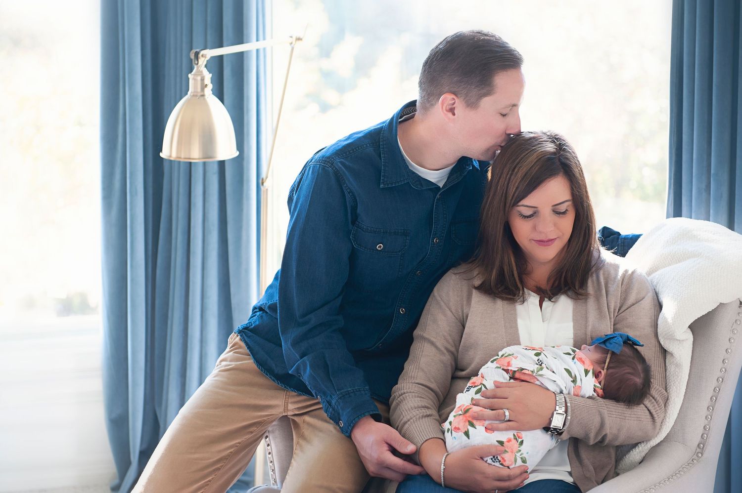 Family gathered around a baby in floral swaddle in a bright blue room.