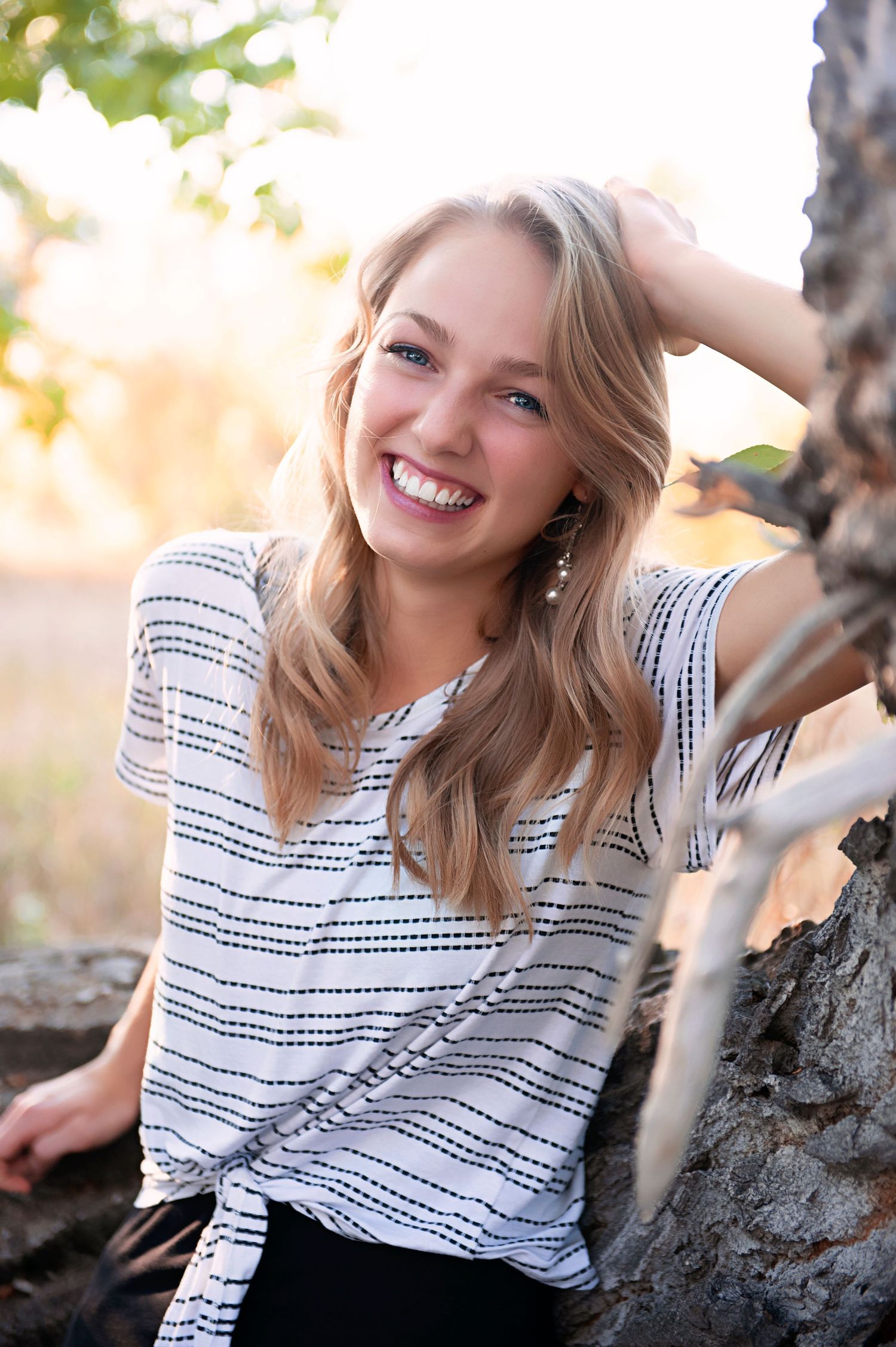 Natural light portrait in striped top against tree background with warm evening glow.