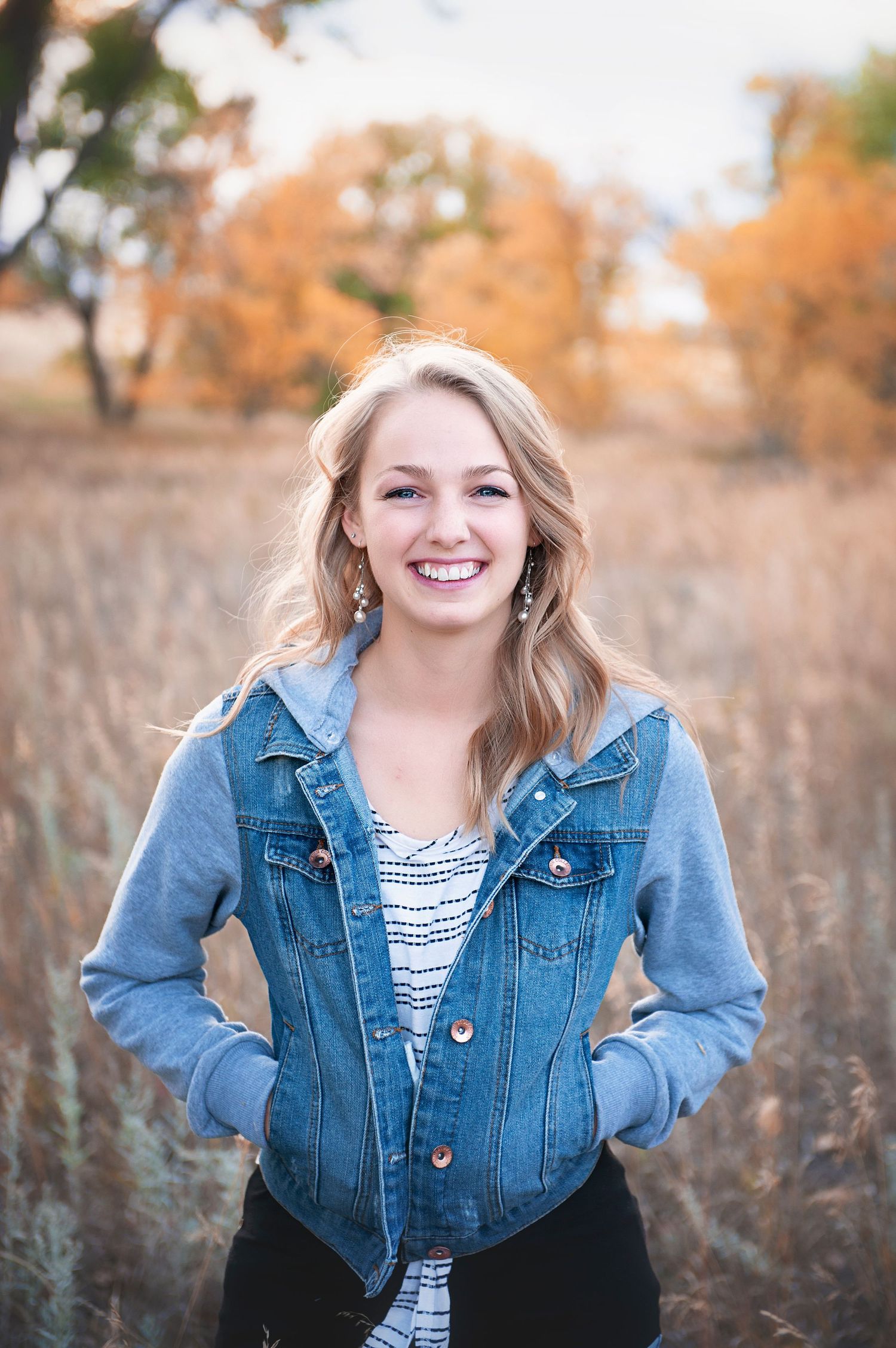 Outdoor portrait in denim jacket and striped top with autumn colors in background.