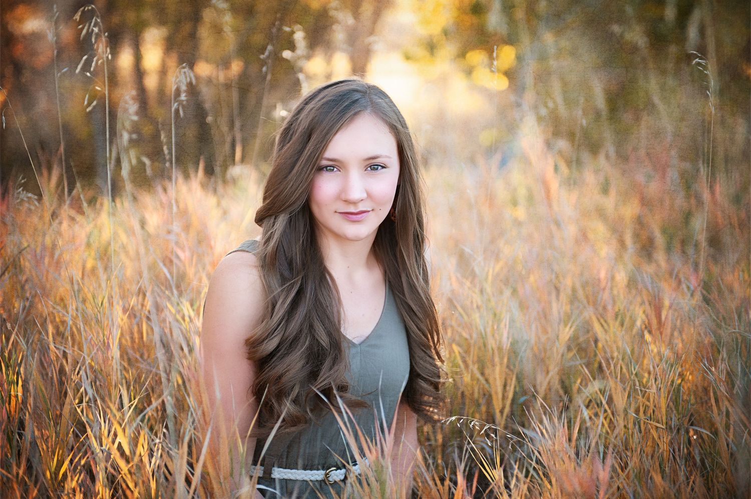 Portrait of a young woman with long brown hair in a natural field setting during golden hour.