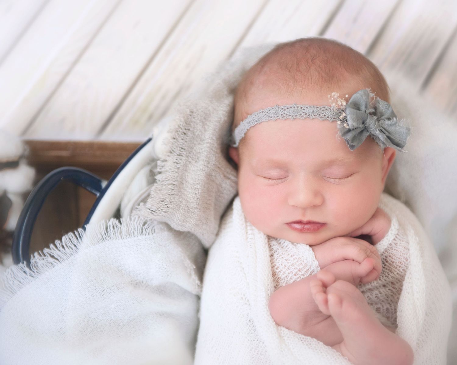 Peaceful sleeping newborn wearing grey headband on soft white blanket.