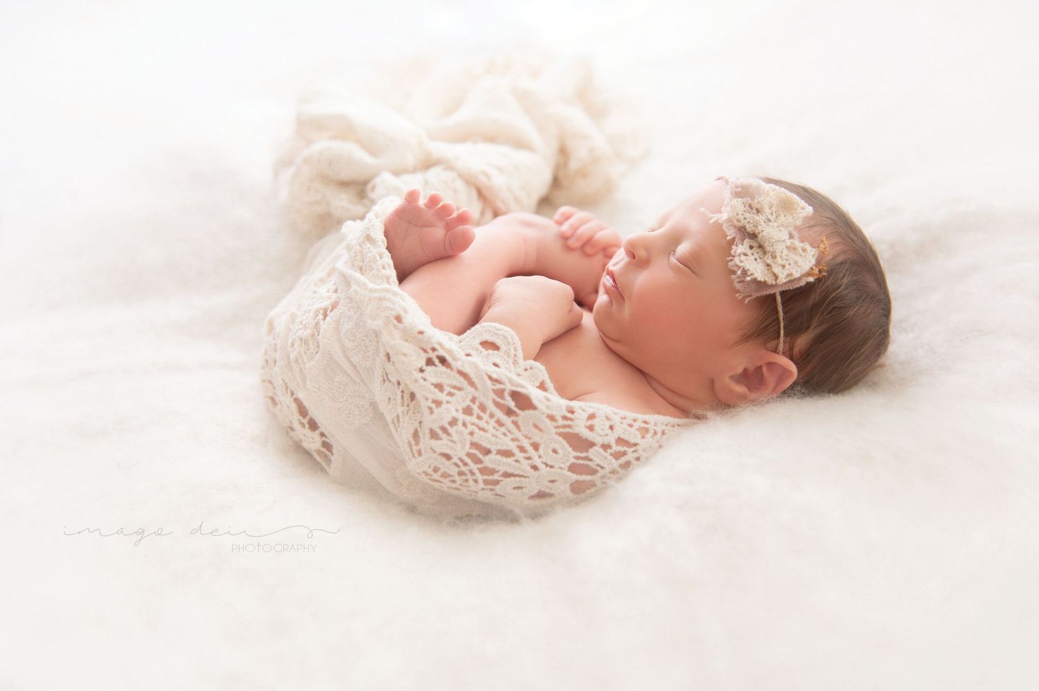 Peaceful newborn resting on soft lace wrap with delicate headpiece.