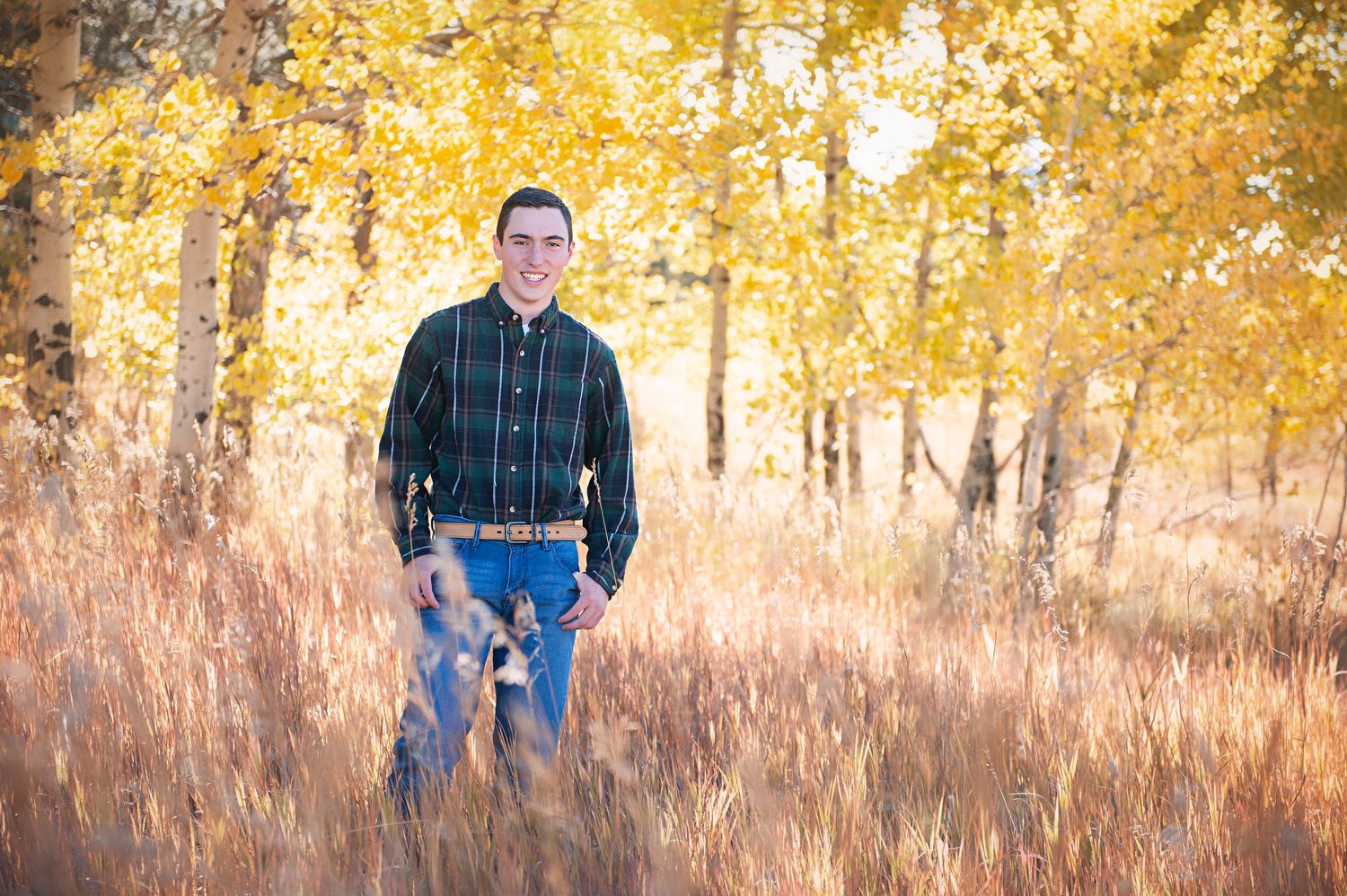 Casual fall portrait among yellow autumn trees wearing plaid shirt and jeans.