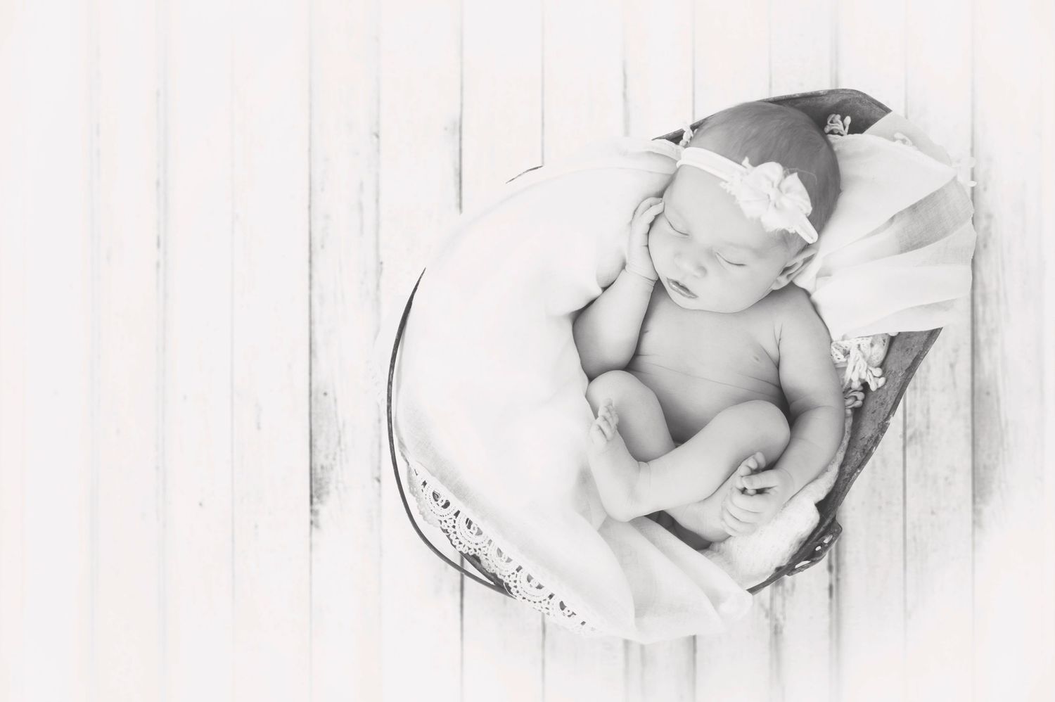 High-key black and white image of newborn baby curled in round basket.