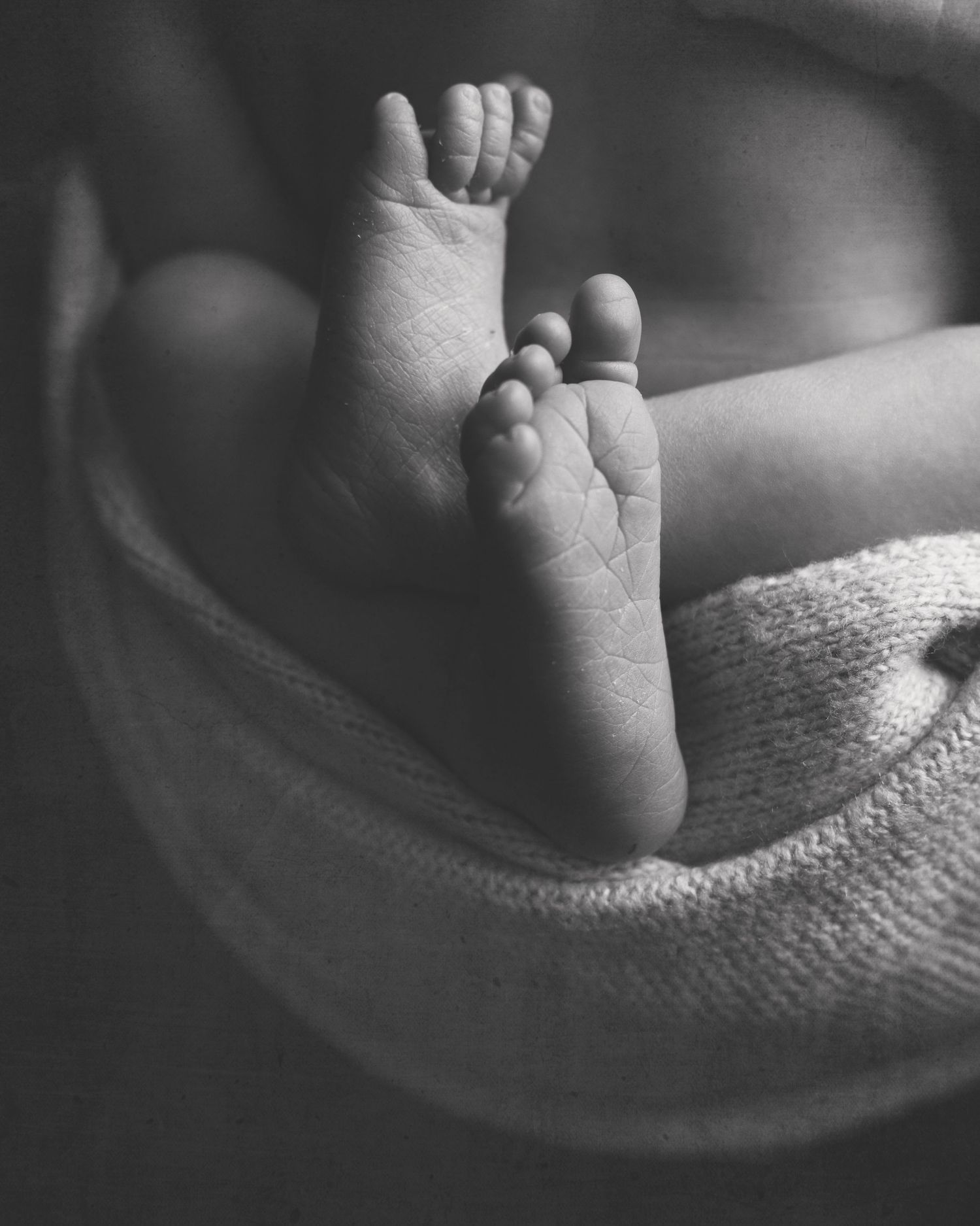 Black and white close-up of tiny baby feet resting on soft fabric.