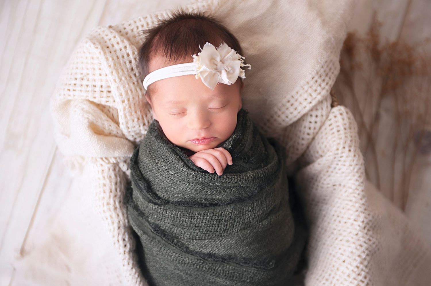 Sleeping newborn wrapped in gray swaddle with white headband on knit blanket.