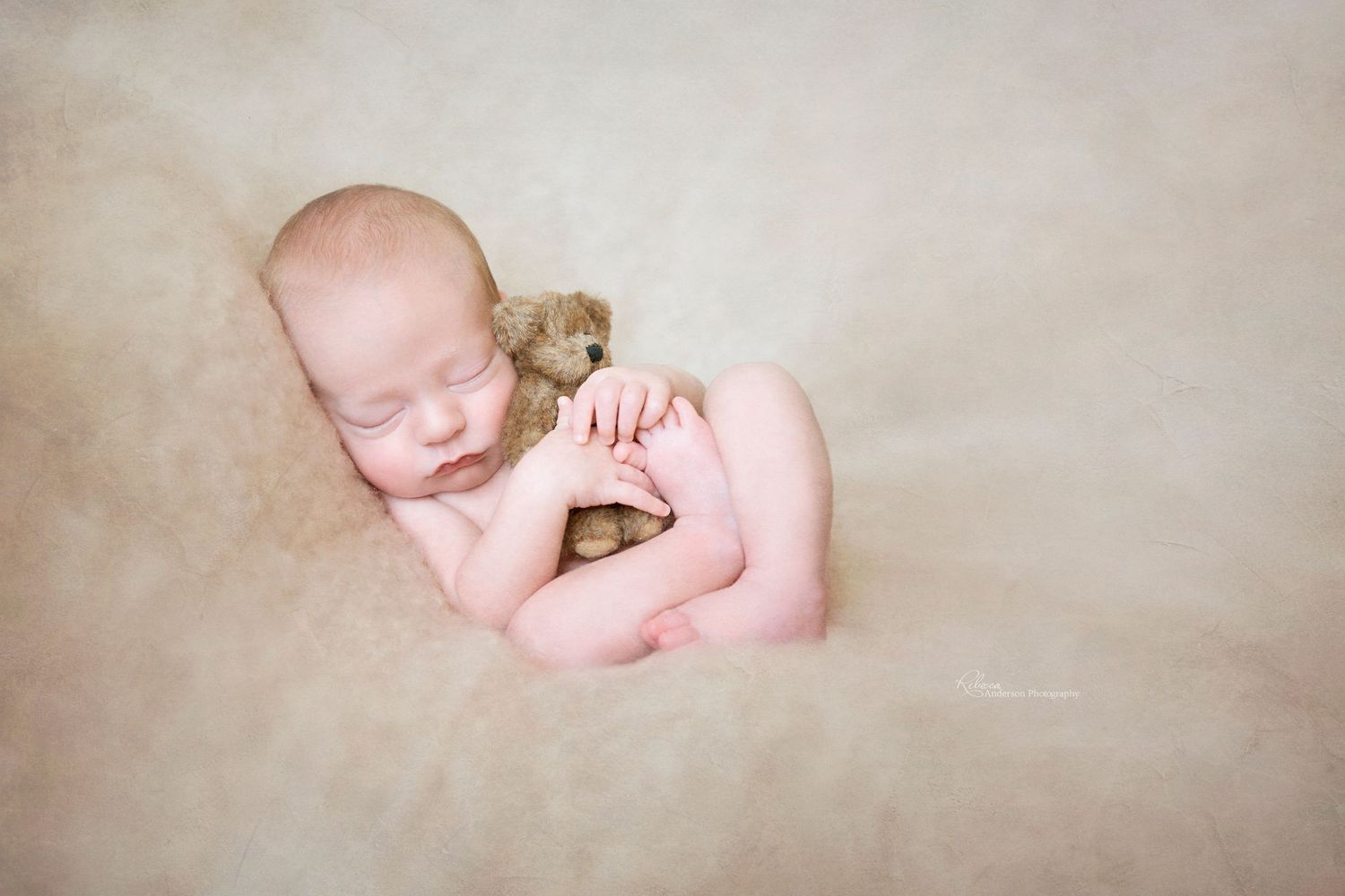 Gentle newborn session featuring baby cuddling small teddy bear on cream backdrop.