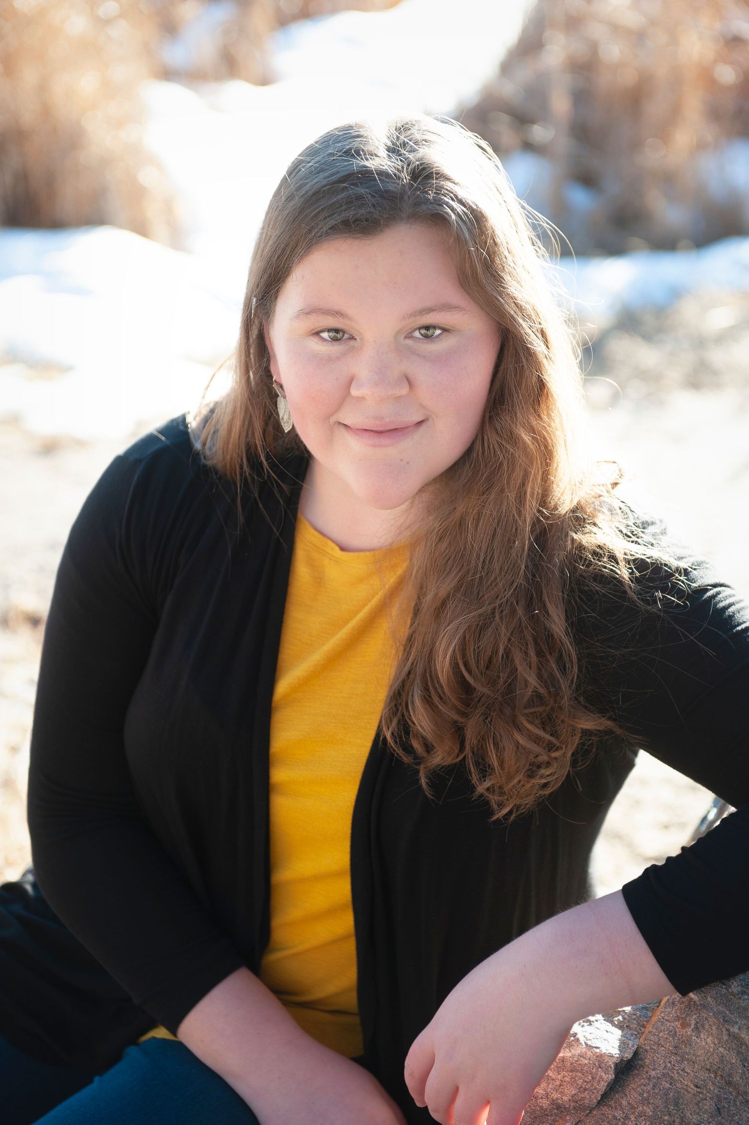 Person in yellow shirt and black cardigan sitting outdoors with snowy background.