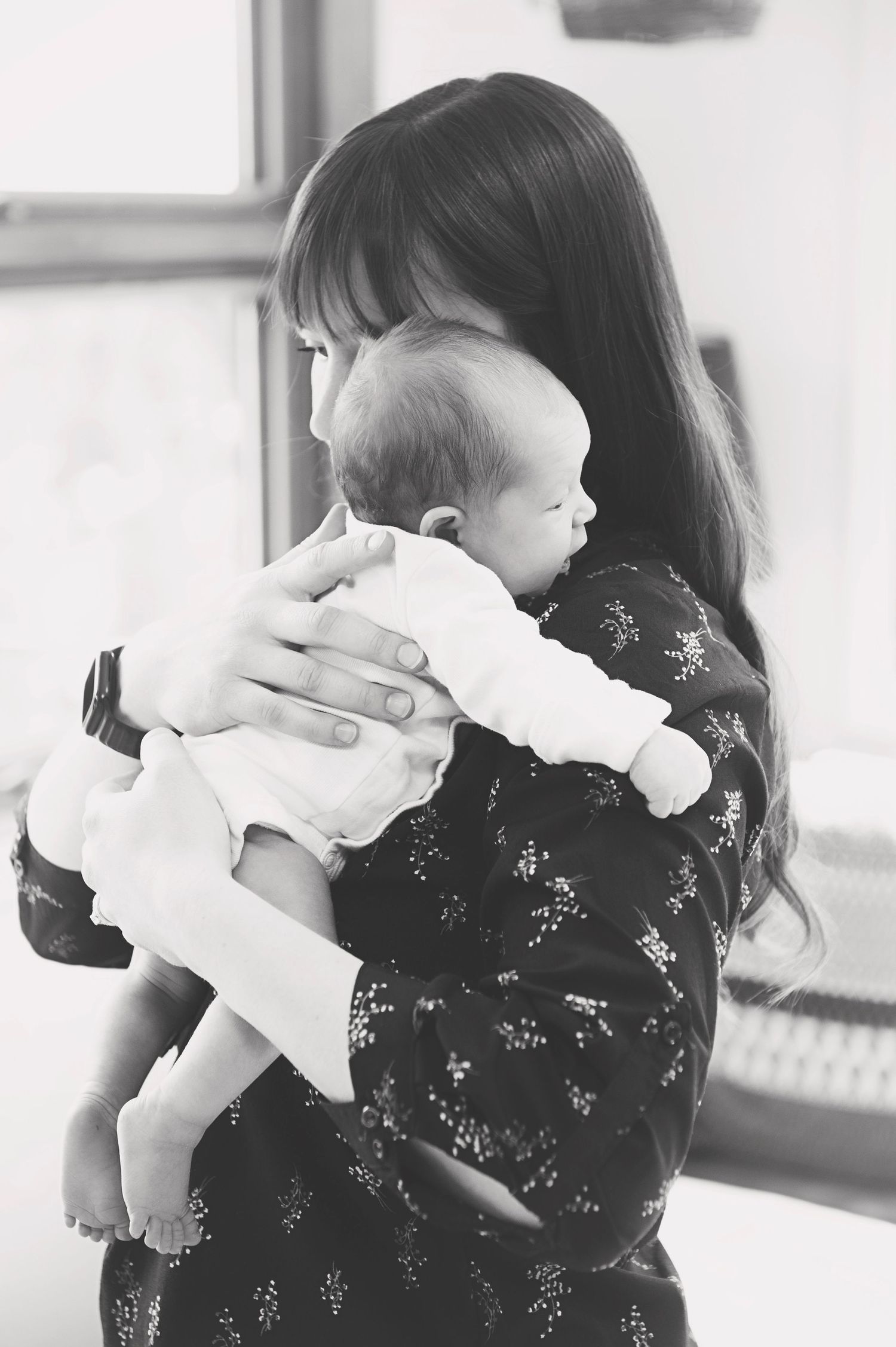 Black and white image of parent holding baby in white outfit against floral dress.