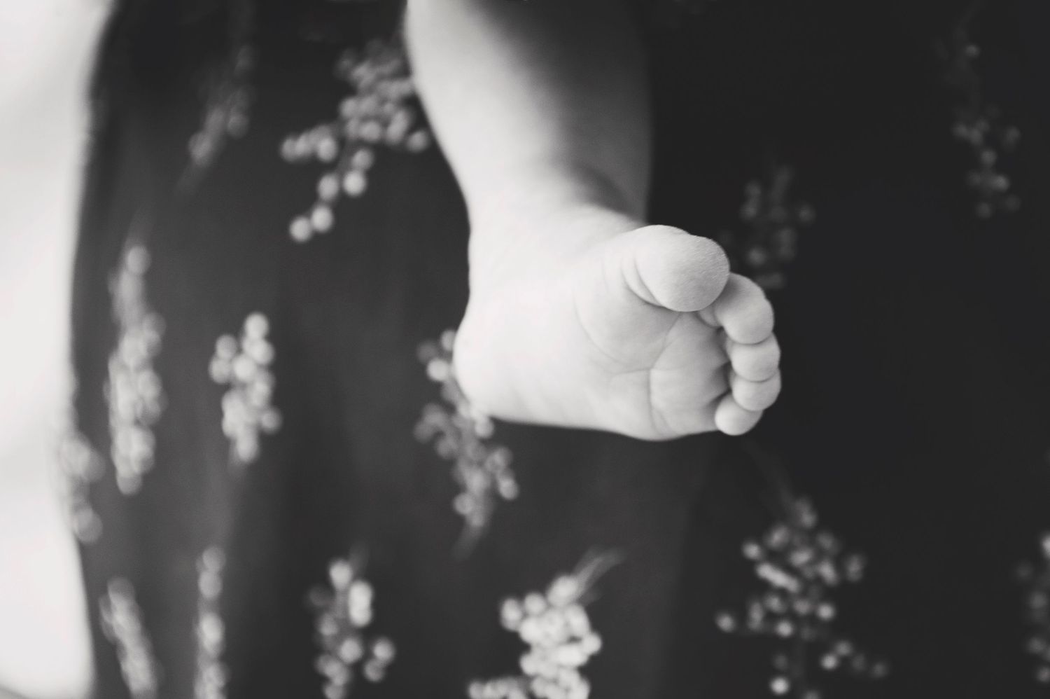 Black and white close-up of tiny baby foot against floral patterned fabric.