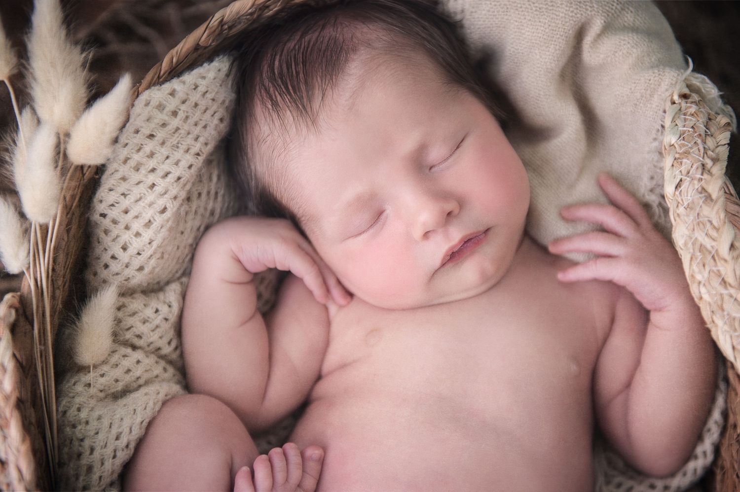 Sleeping newborn nestled in cozy cream knit blankets during professional photo session.