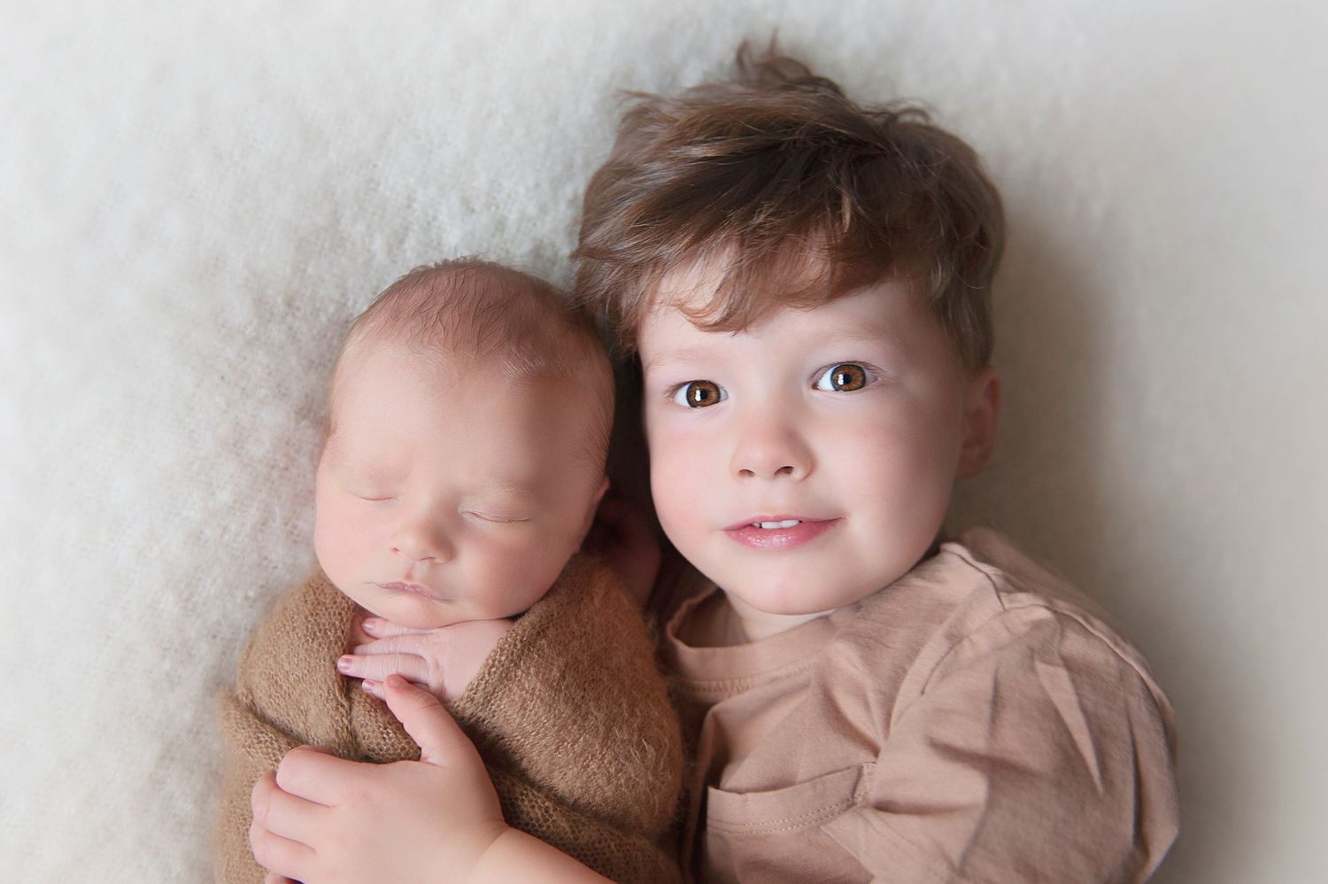 Siblings pose together on beige background during professional photoshoot.