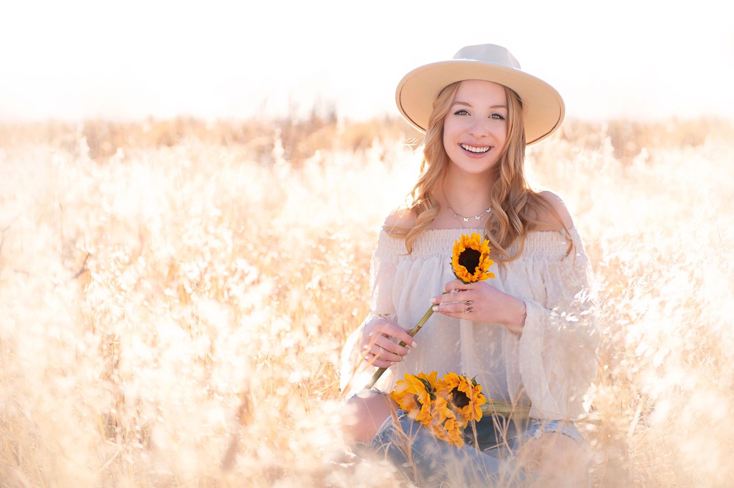 Ethereal sunlit photo in golden field holding bright sunflowers.