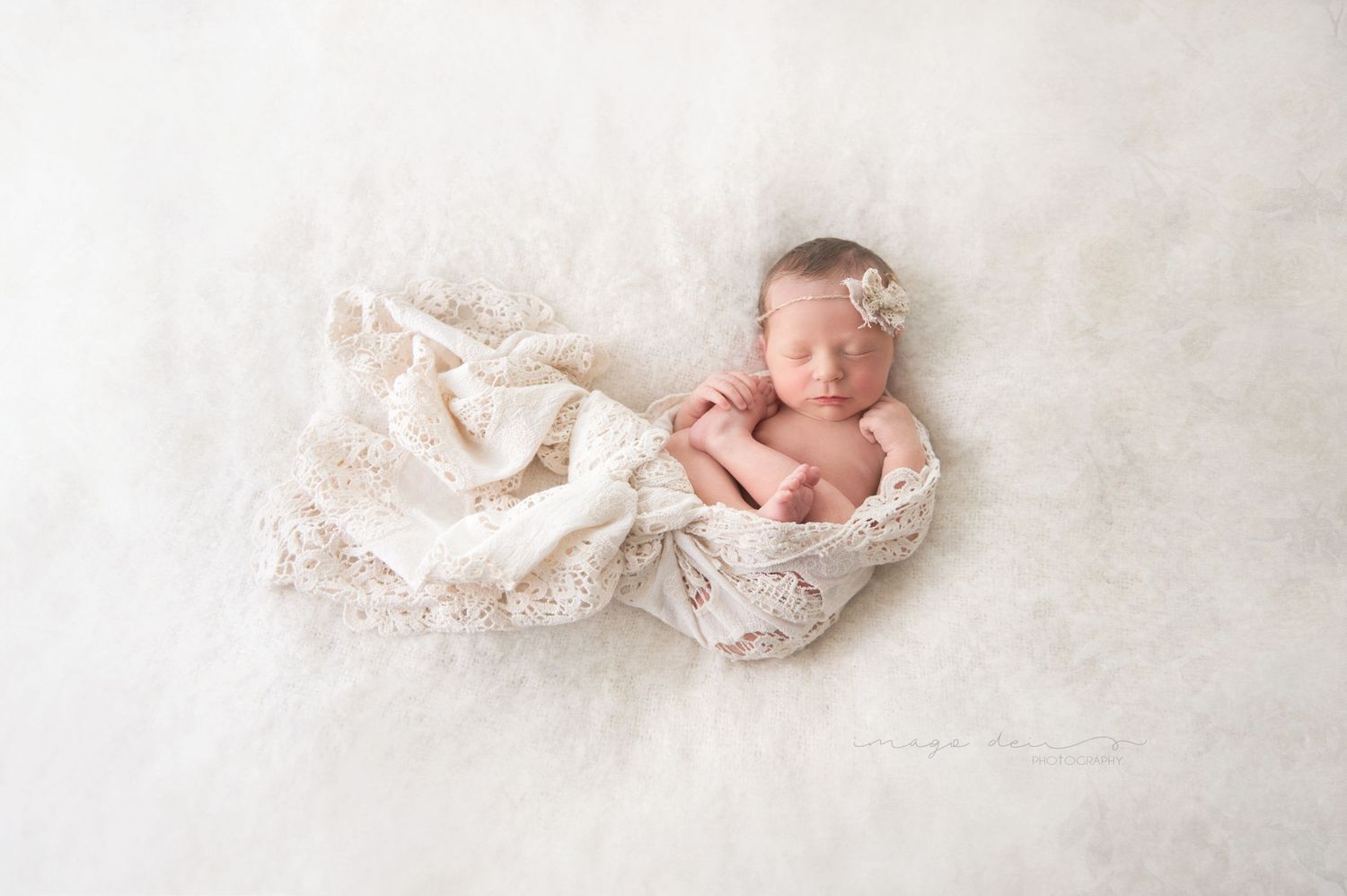 Newborn photography with delicate lace wrapping on white background.