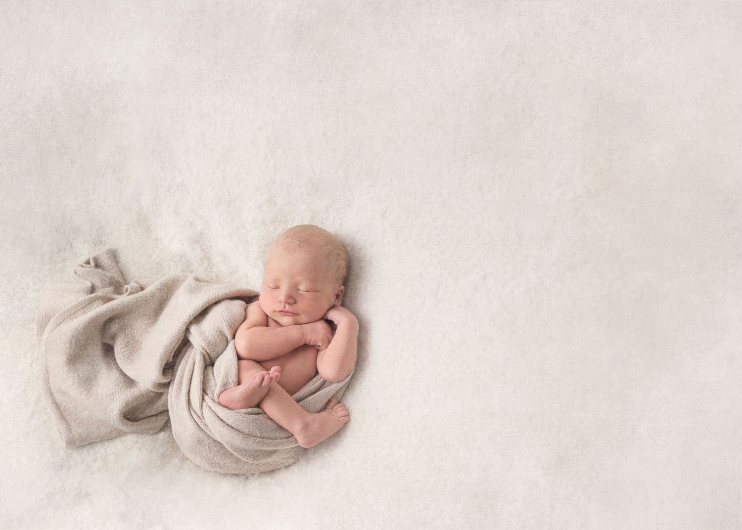 Newborn baby rests peacefully on soft white blankets in minimalist sleeping portrait series.