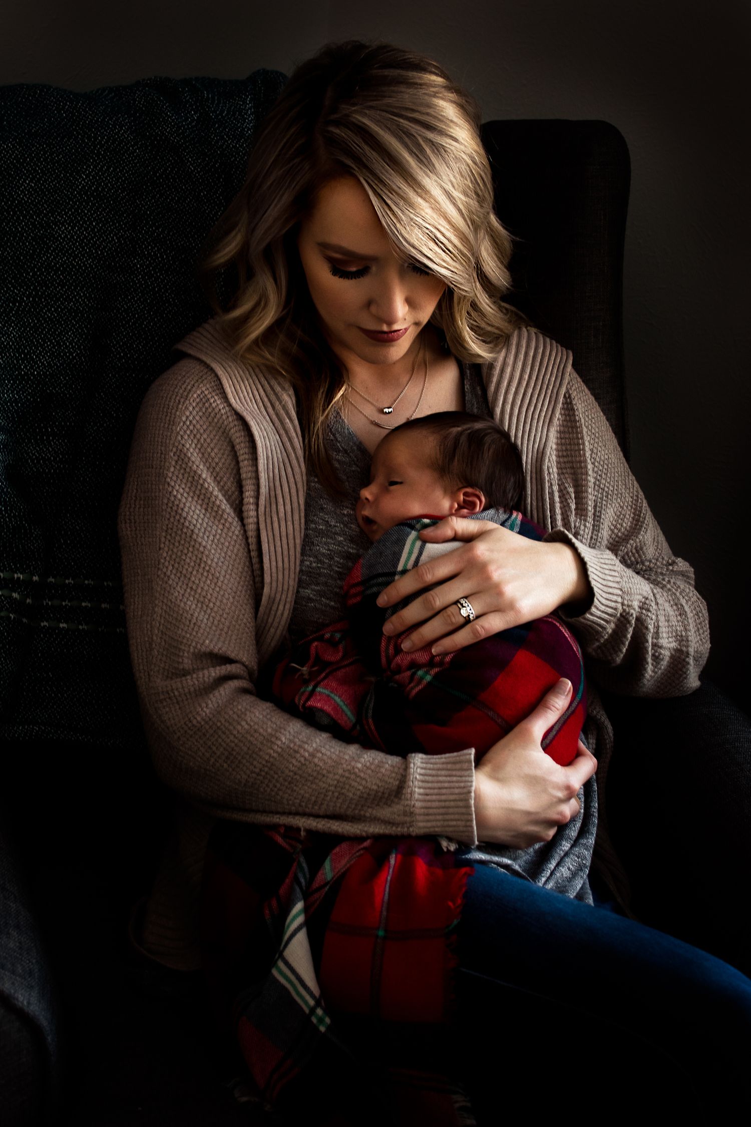 Intimate portrait of tender motherhood moment in moody dramatic lighting.