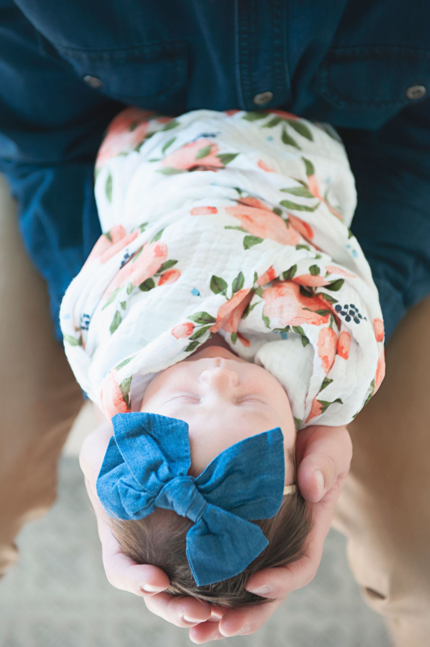 Overhead view of sleeping baby in floral swaddle with blue bow held in hands.