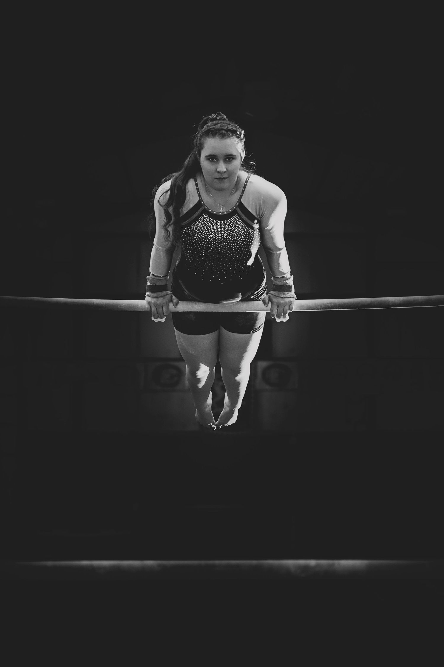 Athletic performer executing a strength move on gymnastics equipment in dramatic monochrome.