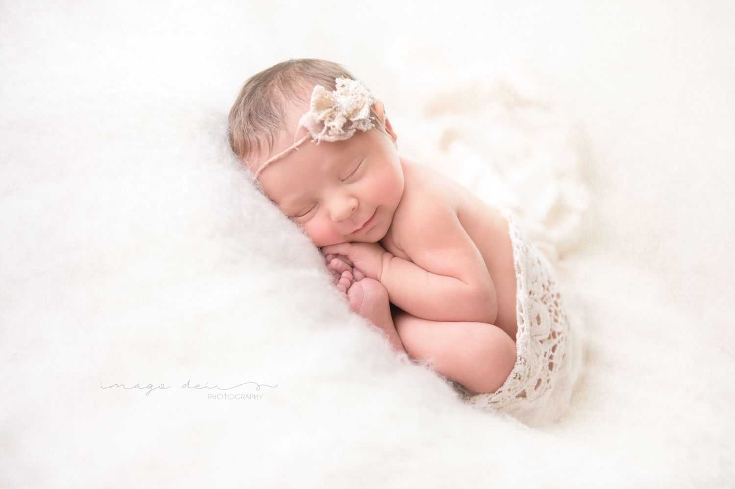Artistic newborn photography with soft white lace and delicate hair accessory.