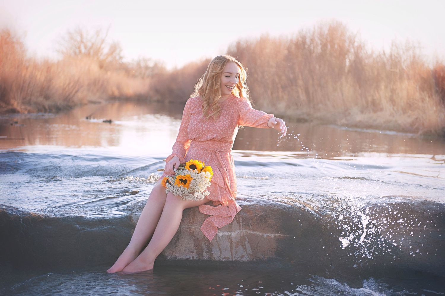 Person in pink dress sitting on rock creates splash in river during sunset.
