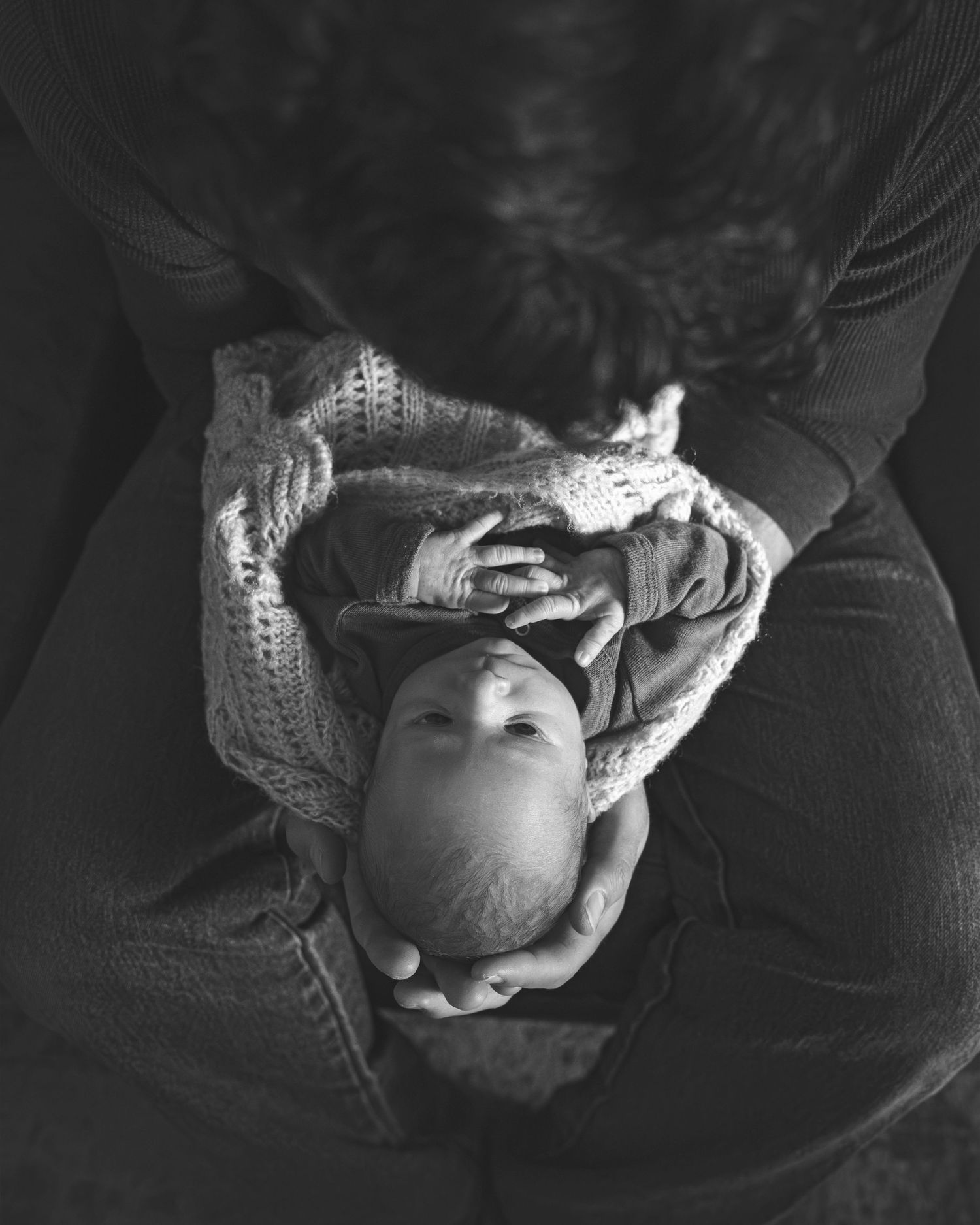 Black and white portrait of a baby wrapped in knit fabric, captured from above.
