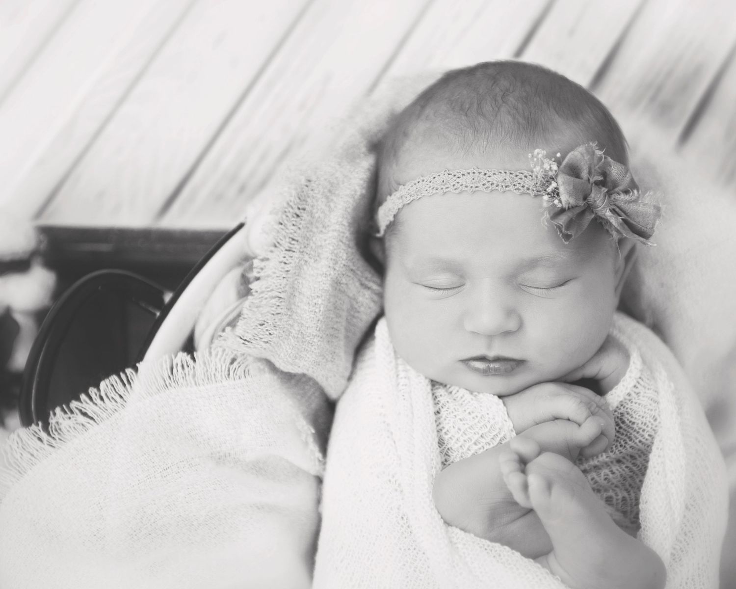 Black and white portrait of sleeping newborn wearing lace headband wrapped in blanket.