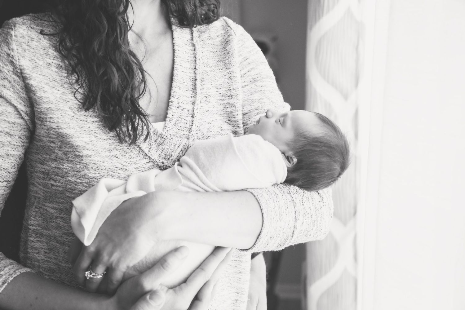 A gentle black and white portrait of someone holding a sleeping newborn.