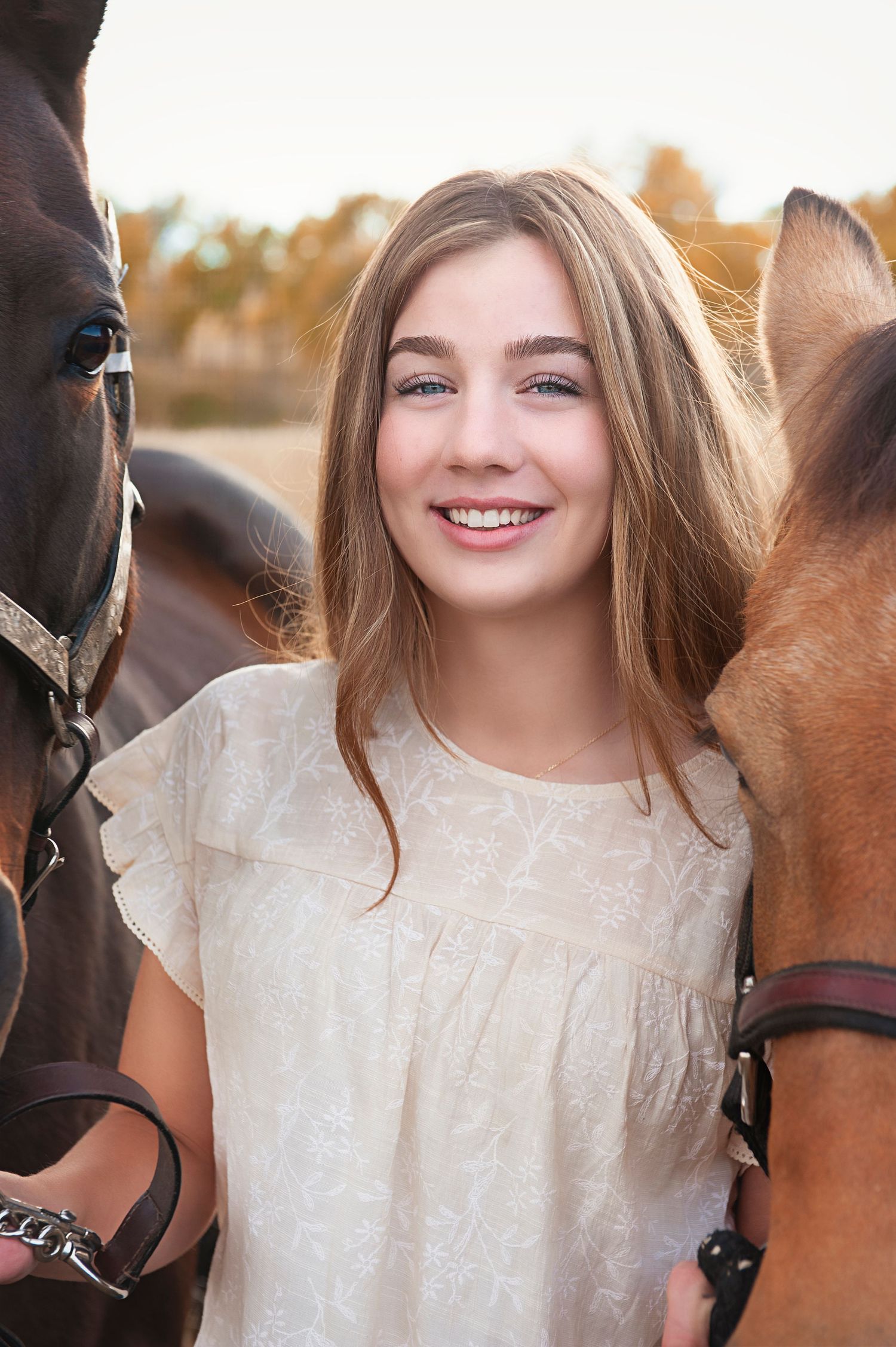 Person in white blouse between two horses looking at camera.